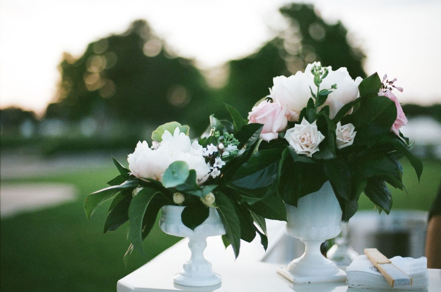 White floral centerpiece arrangements in elegant pedestal vases set on outdoor table at dusk.