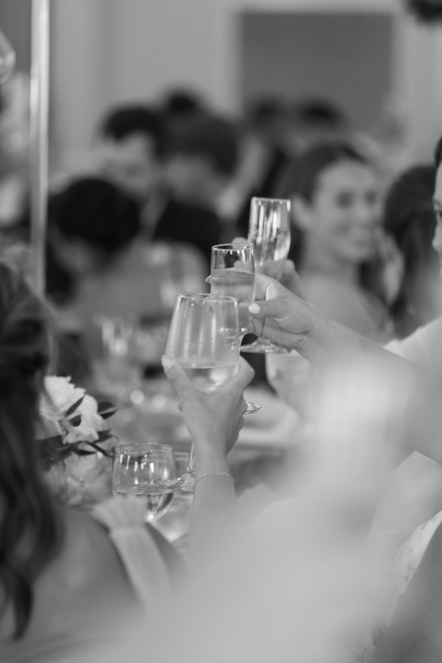 Black and white image of champagne glasses clinking during a wedding toast.