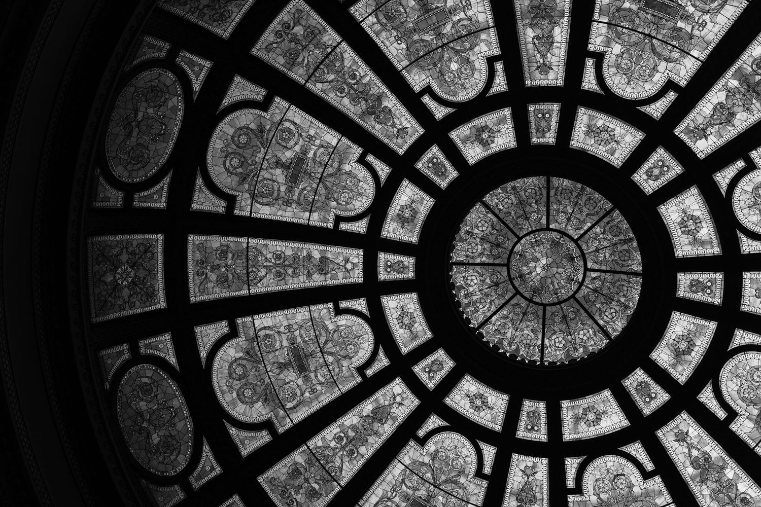 Black and white architectural photograph of an ornate domed glass ceiling with geometric patterns.