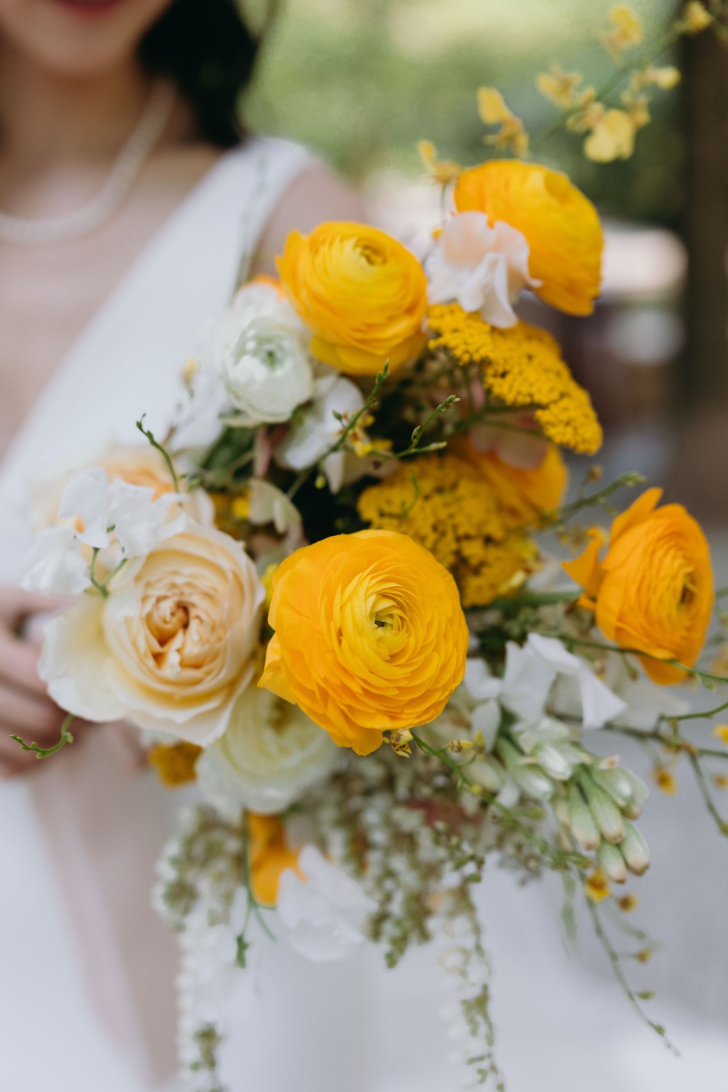 Close-up of vibrant yellow and white wedding bouquet featuring ranunculus and delicate greenery.