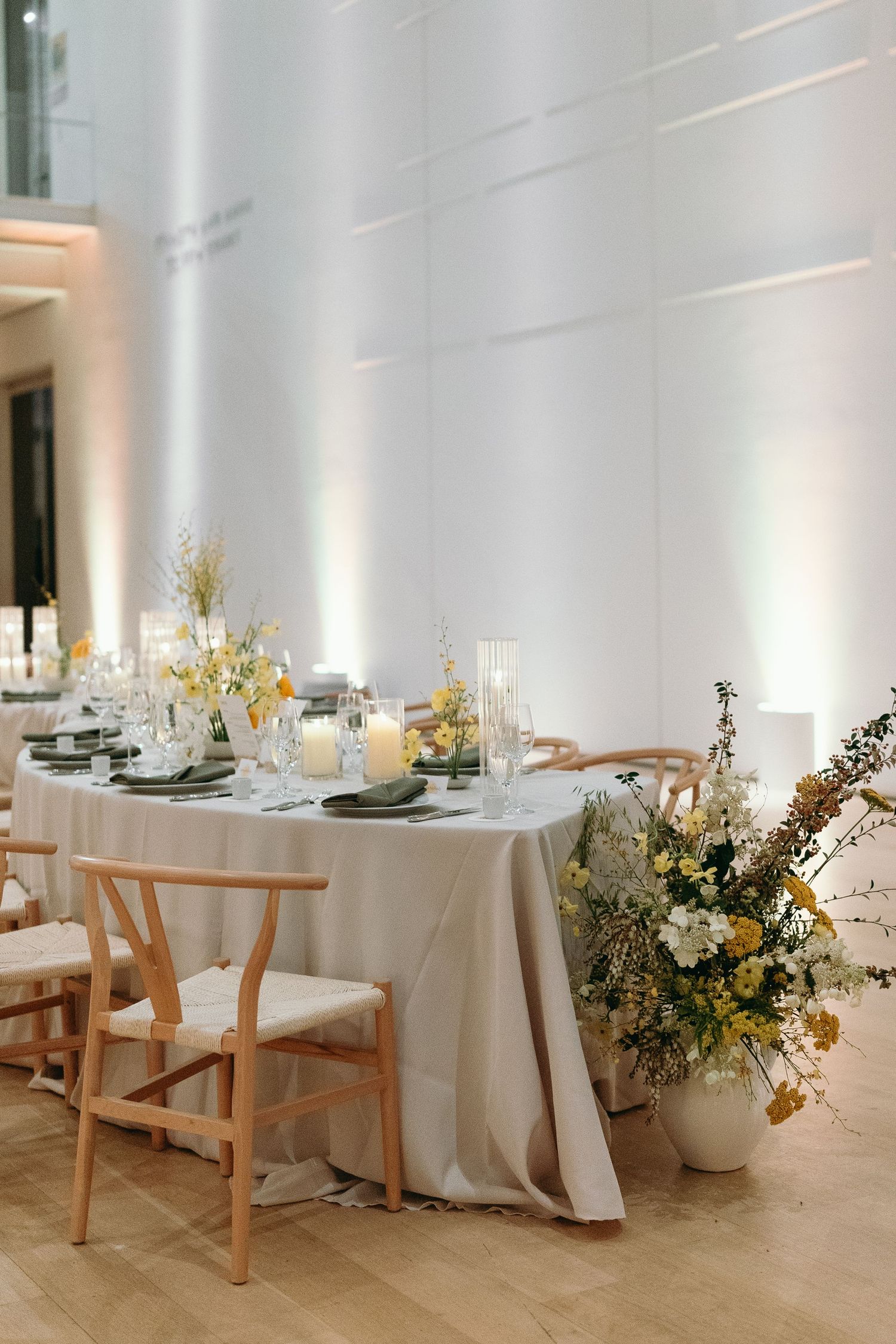 Elegant wedding table setting with wooden chairs and lush floral arrangements in white and yellow.