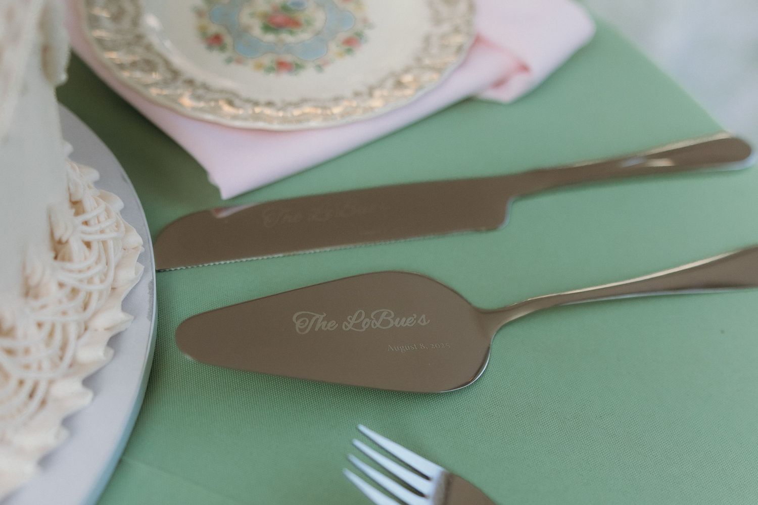 Personalized silver cake server and knife set on a mint green napkin at an elegant wedding table setting.