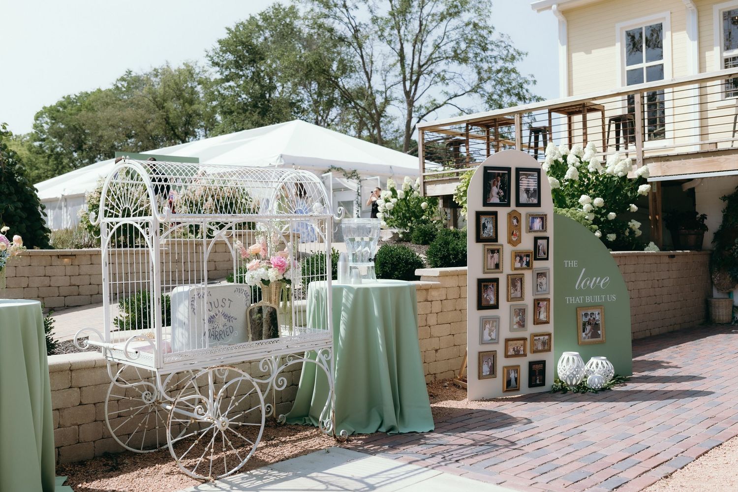 Elegant outdoor wedding display with white ornate carriage, mint green tablecloth, photo wall, and floral arrangements on brick patio.