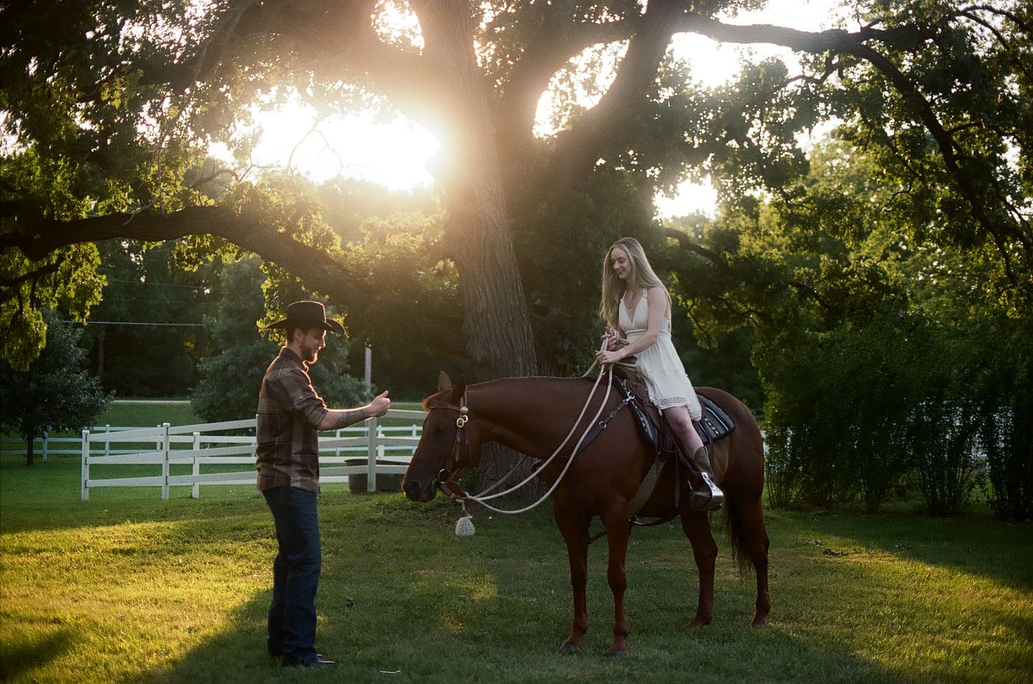 Golden sunset illuminates an outdoor horse riding lesson at a tranquil farm with white fencing and autumn trees.