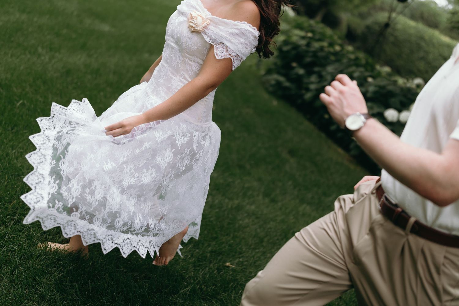 A couple dances together outdoors in wedding attire, spinning and twirling on green grass.