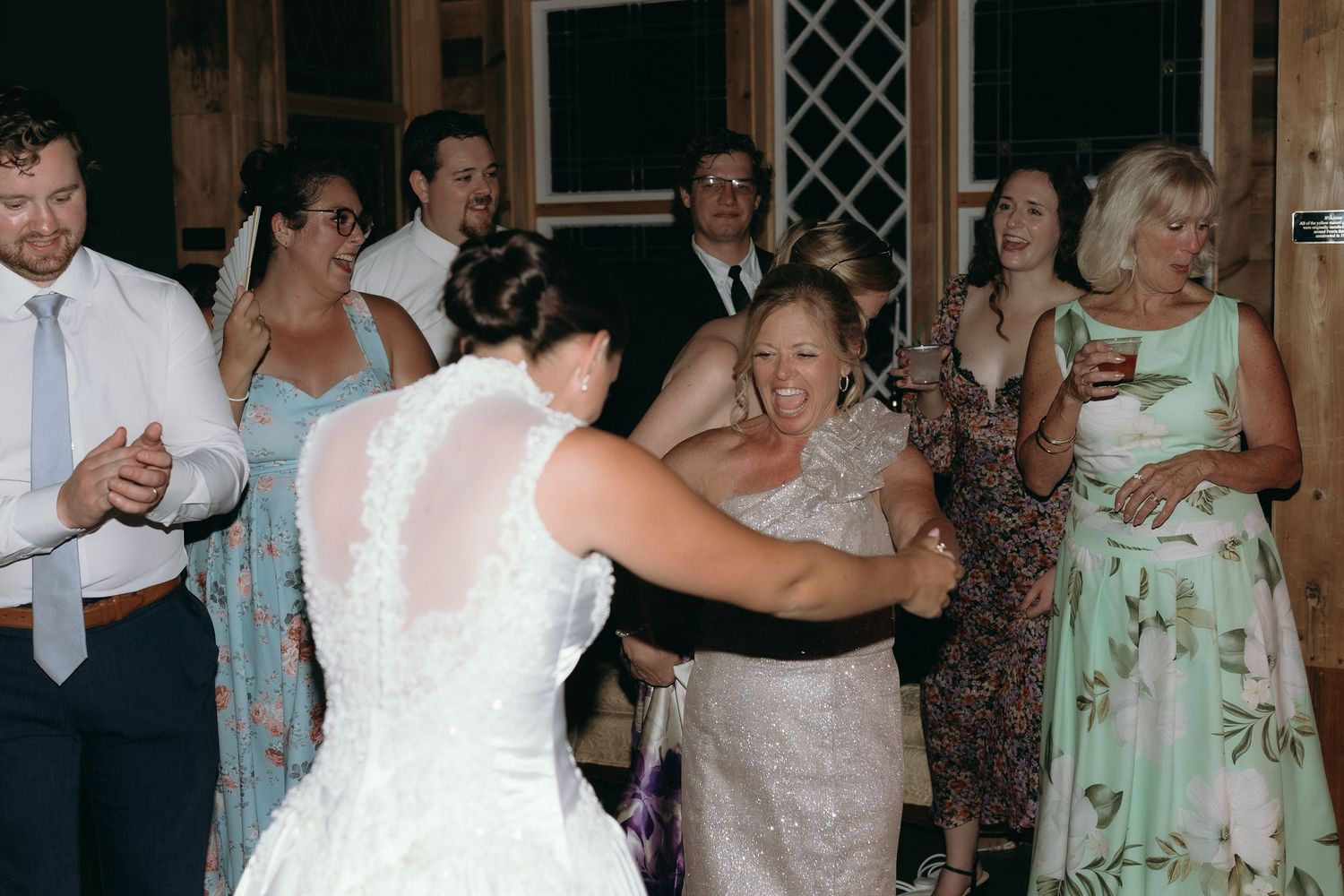 Bride in lace gown hugging a guest while others watch and clap on the wedding dance floor.