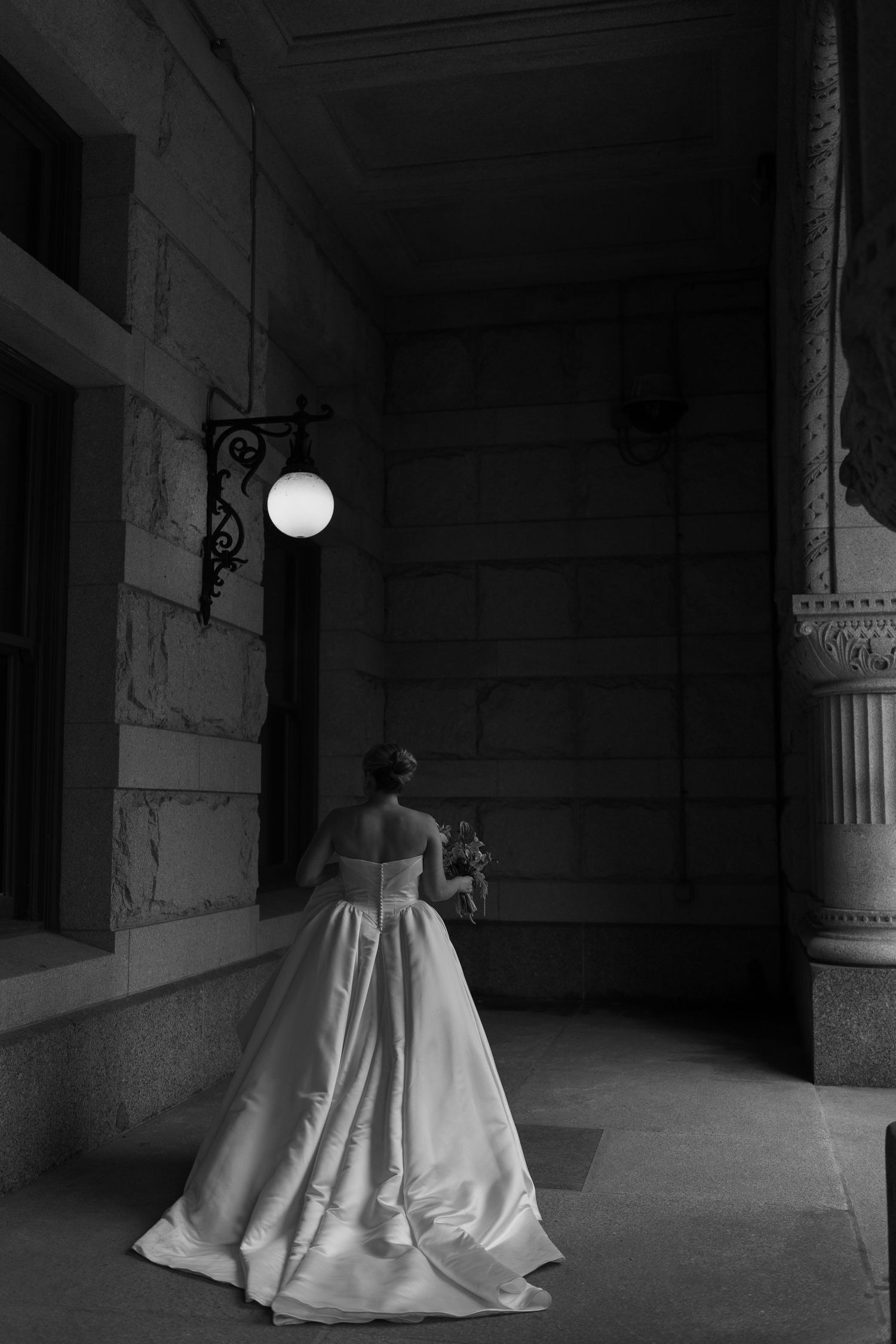 A black and white series of photos showing a bride's white wedding dress flowing across a dark stone corridor.