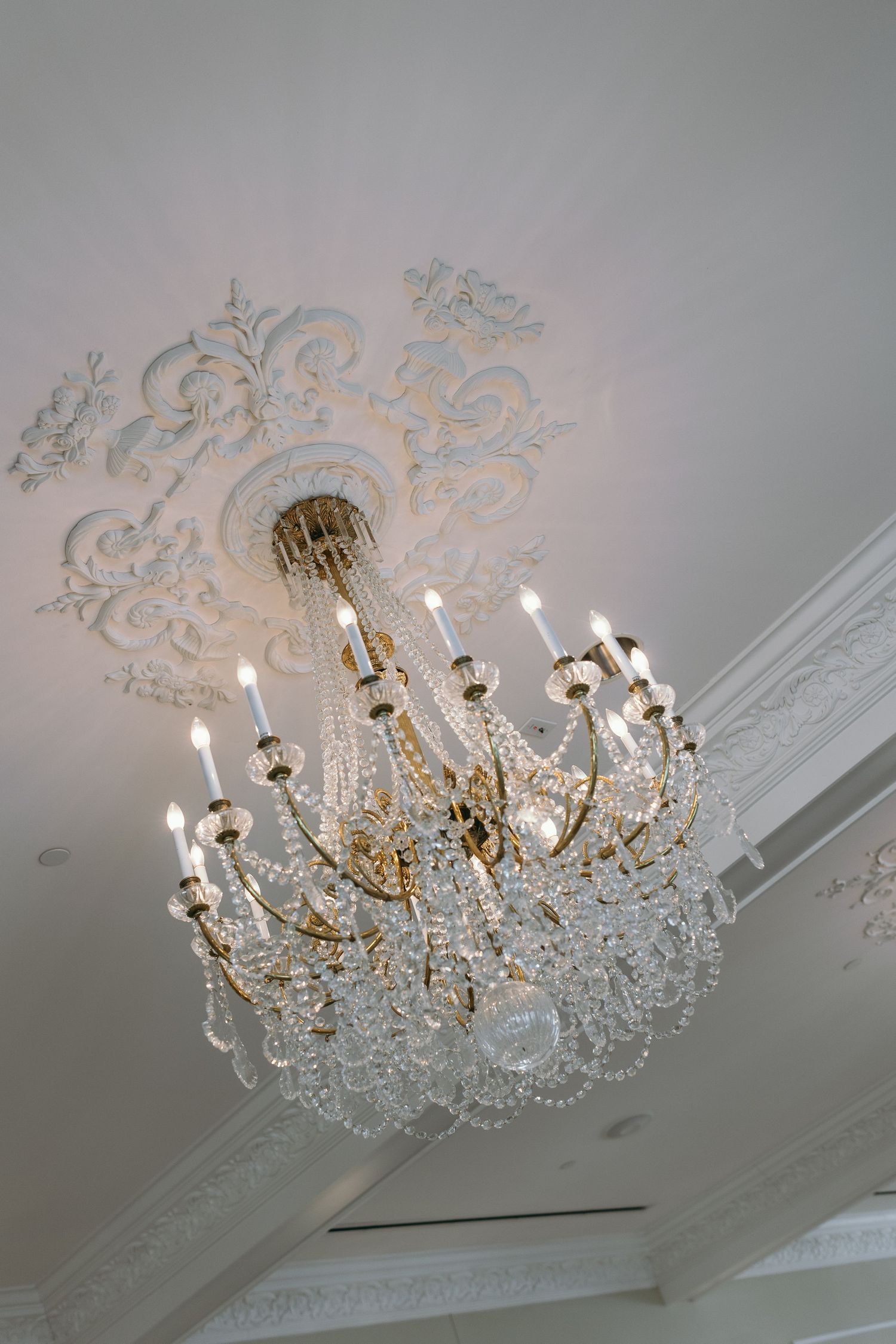 Elegant crystal chandelier with ornate ceiling medallion creates luxurious ambiance in classic interior space. Wedding venue details