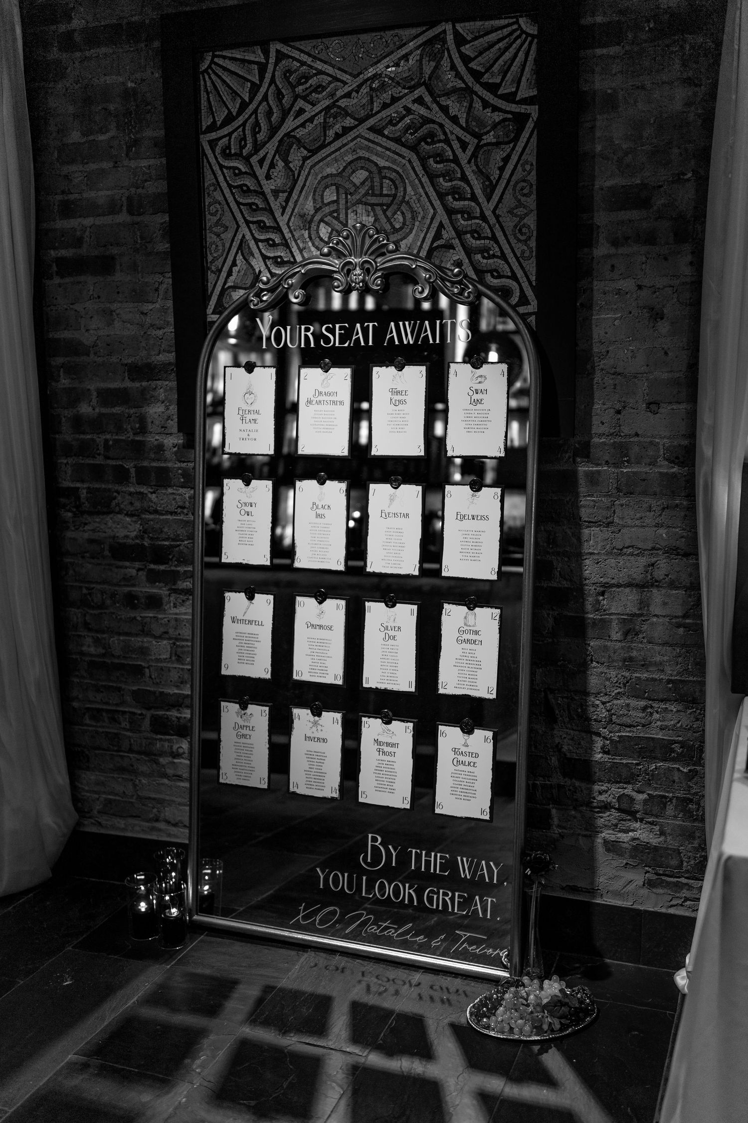 Seating chart display with papers arranged on ornate dark wall at wedding venue.
