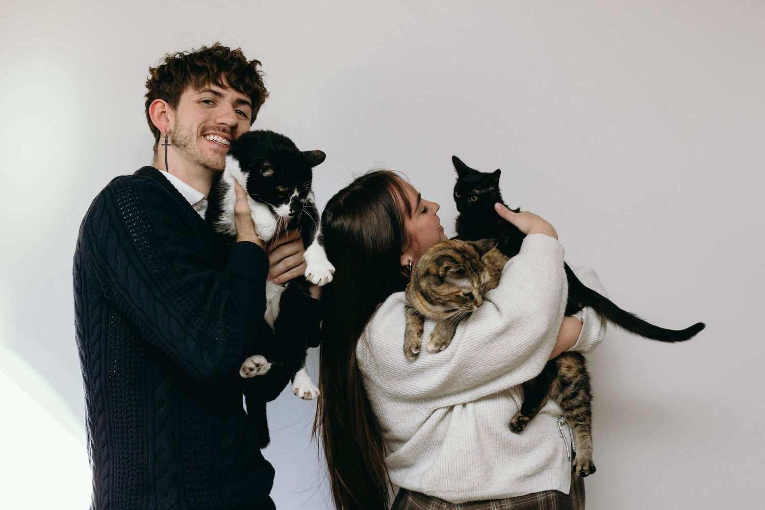 A couple plays with their cat in a series of playful poses against a white background.