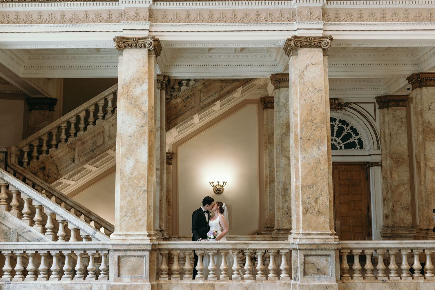 A romantic wedding portrait on a grand marble staircase with classic architectural columns.
