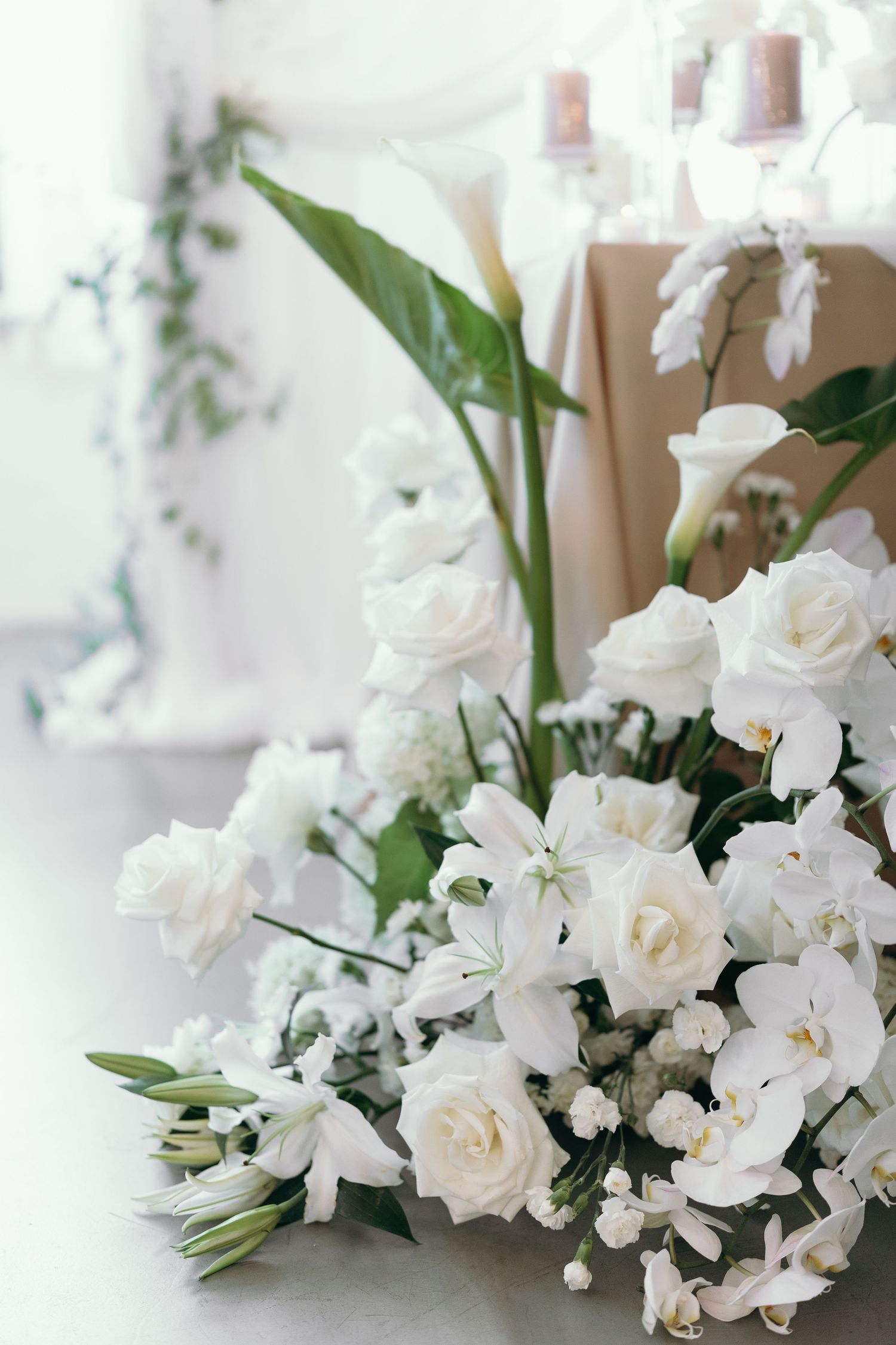 Elegant white floral arrangement with roses, orchids and greenery on light background.