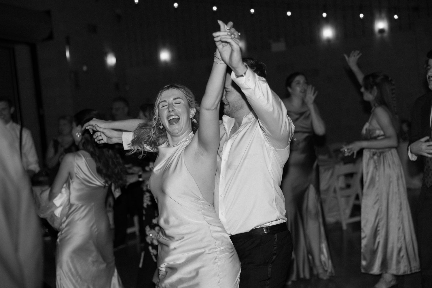 Black and white photo of a joyful couple dancing together at a wedding reception celebration.