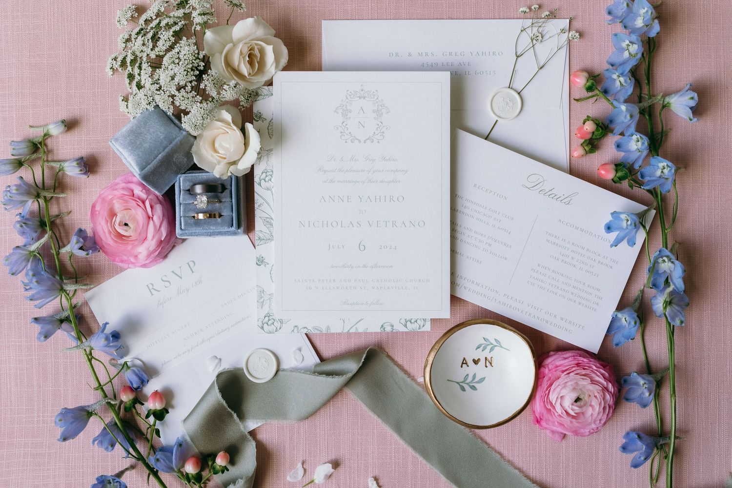 Wedding invitation suite with pink and blue flowers, ribbons, and delicate styling on pink background.