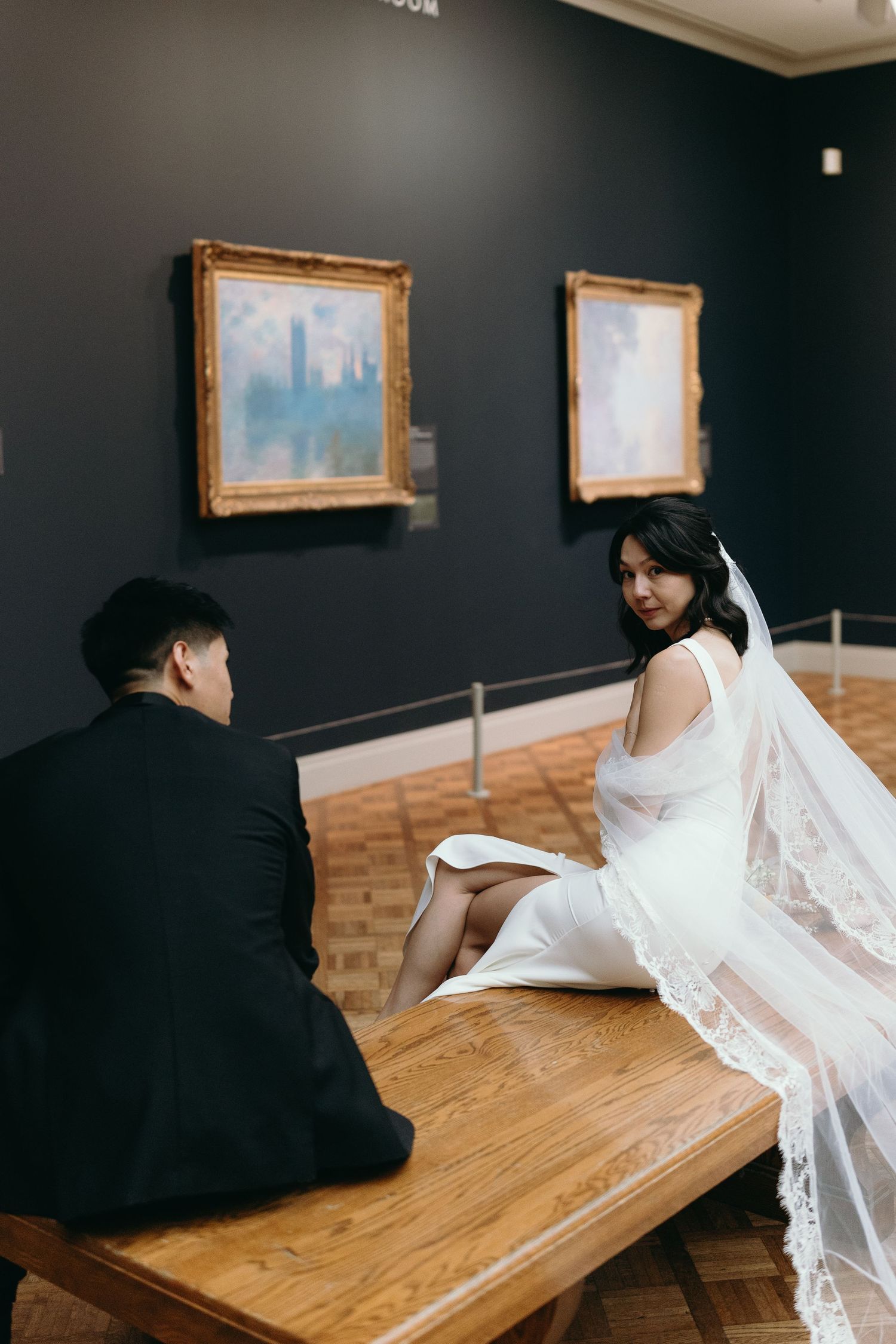 A couple sharing a moment in an art gallery with framed paintings on dark walls.