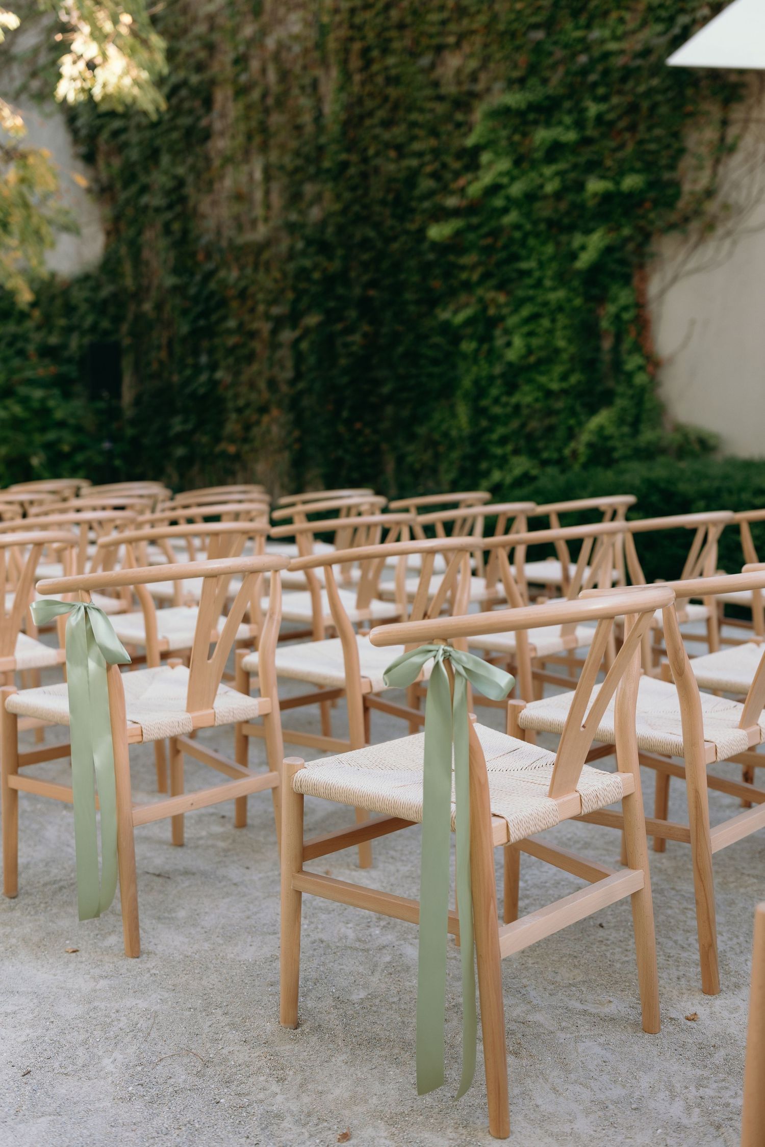 Wooden ceremony chairs with mint green ribbons arranged in rows outdoors.