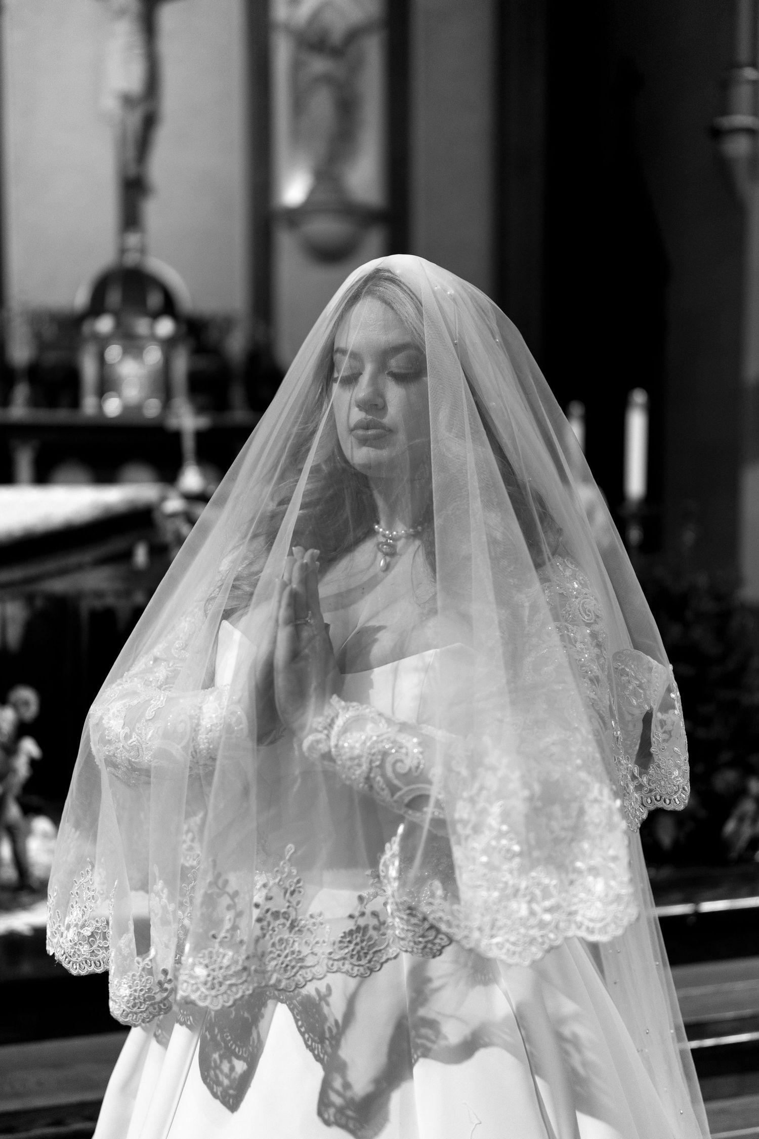 A delicate lace veil drapes over a wedding dress in a black and white church setting.