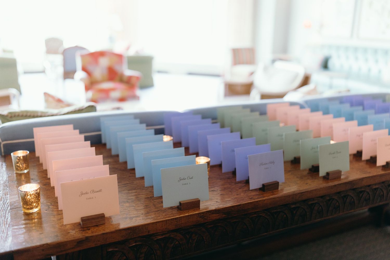 Rows of pink and blue place cards arranged on a wooden surface with tealights.