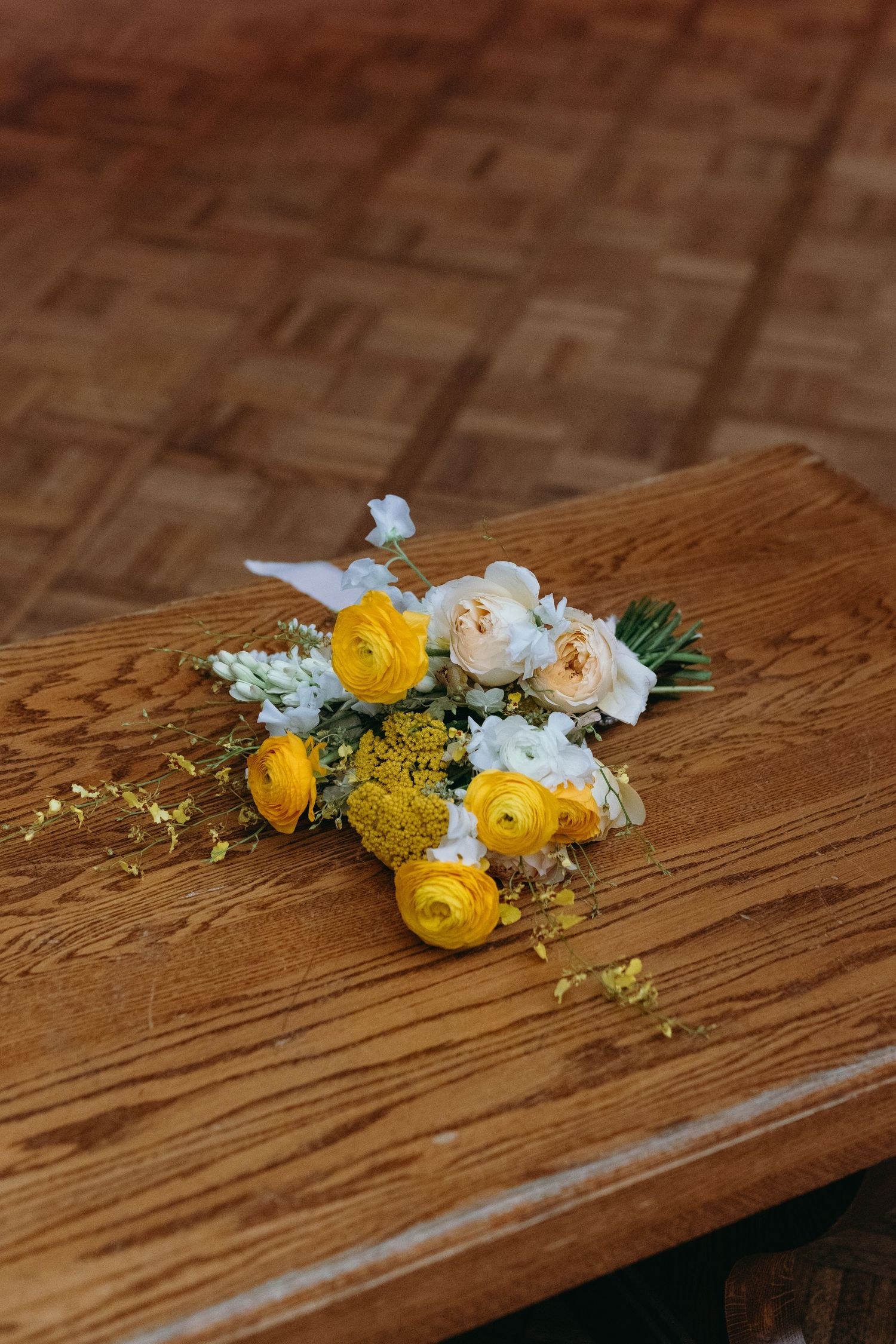 A delicate bouquet of yellow ranunculus and white flowers arranged on a rustic wooden table.