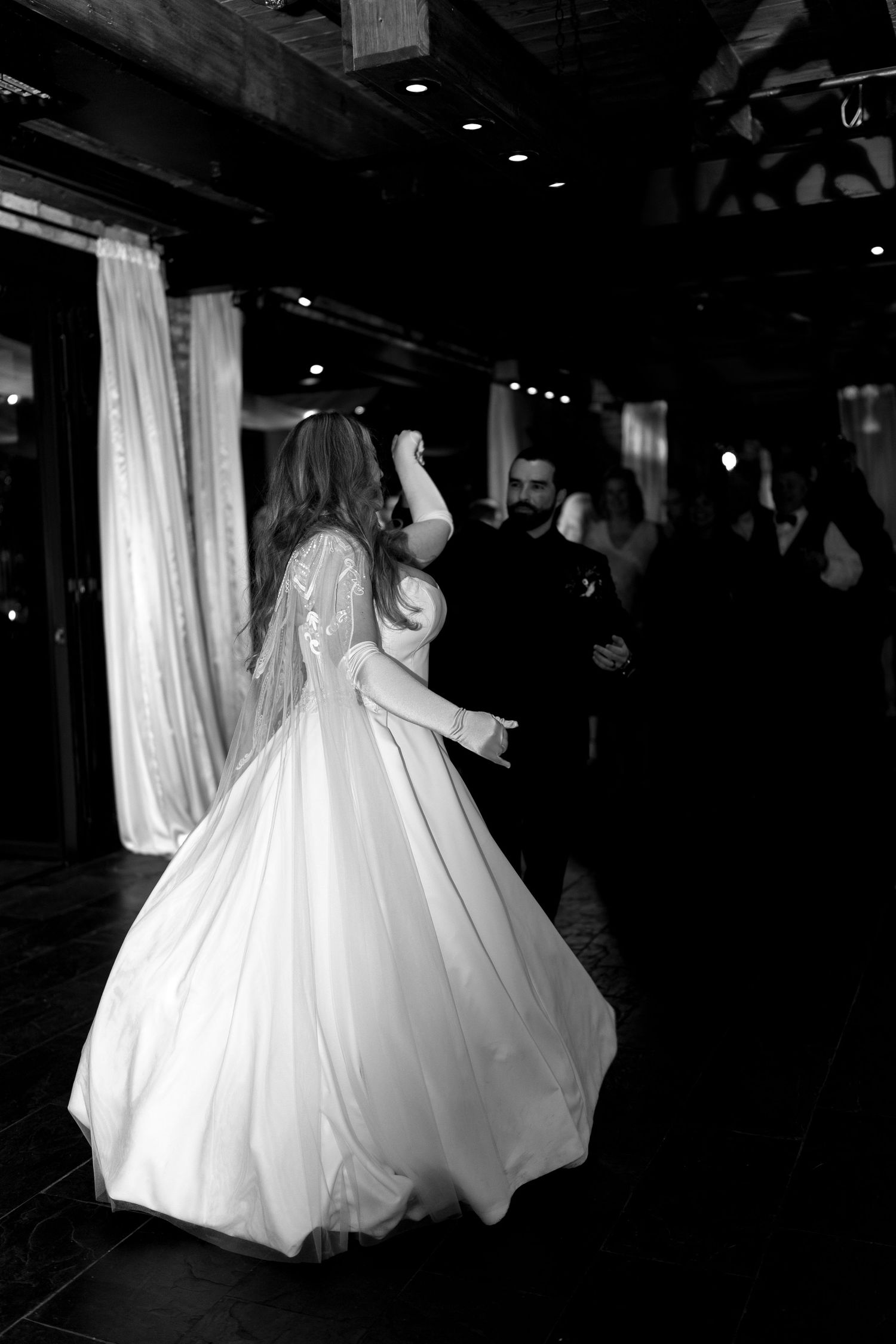 Black and white photo of couple dancing in ballroom, bride wearing full ball gown.