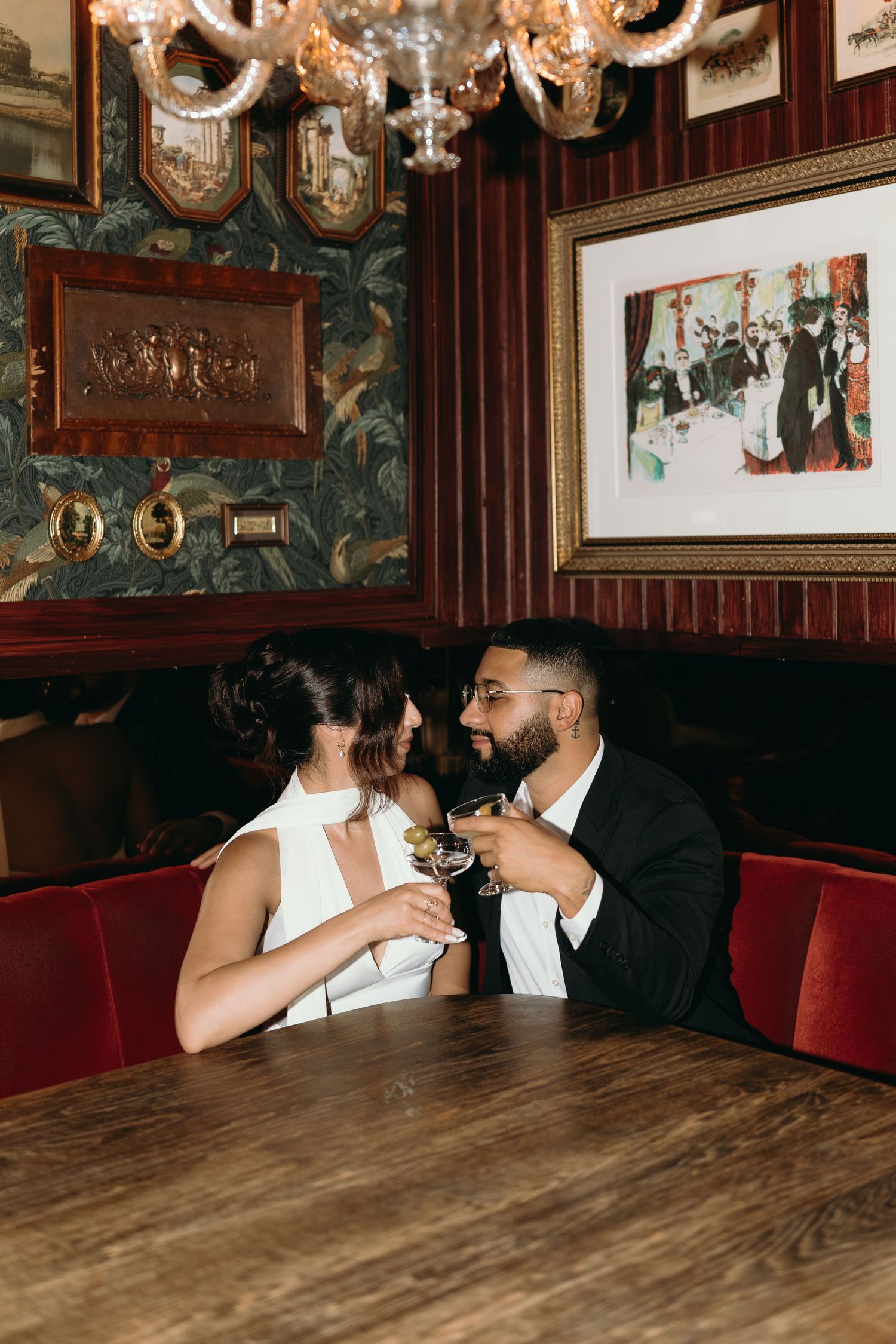 Couple enjoying drinks in an ornate vintage-style restaurant with chandelier and artwork.