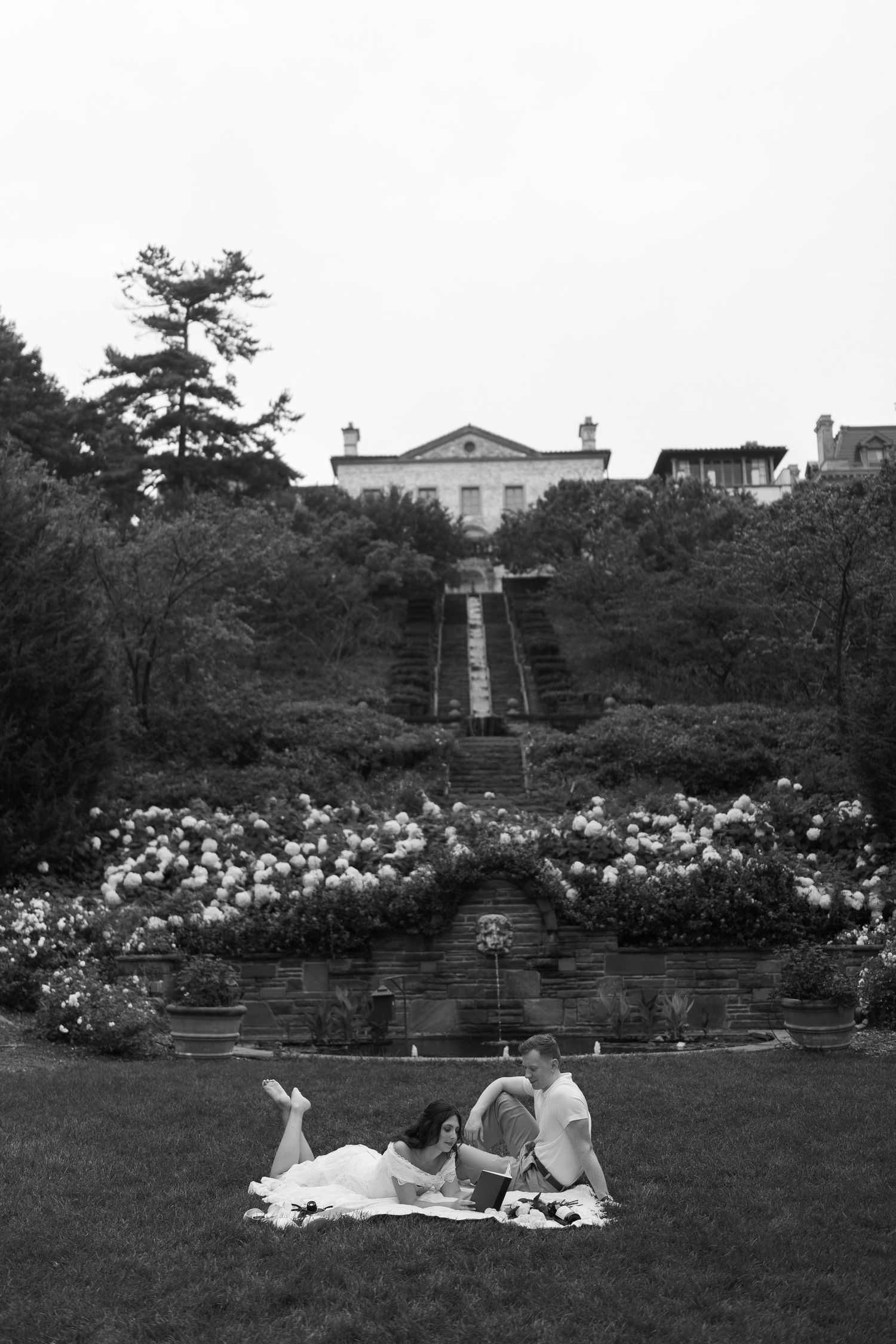 A picnic setup on manicured lawn with grand stone staircase and flowering gardens in background.