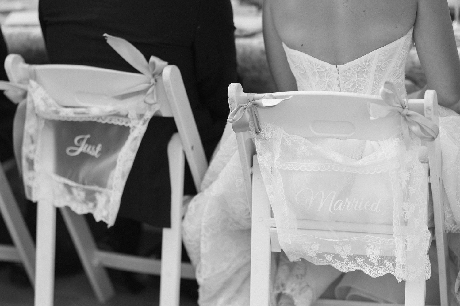 Black and white photo of Just Married signs on white chairs at an elegant outdoor wedding ceremony.