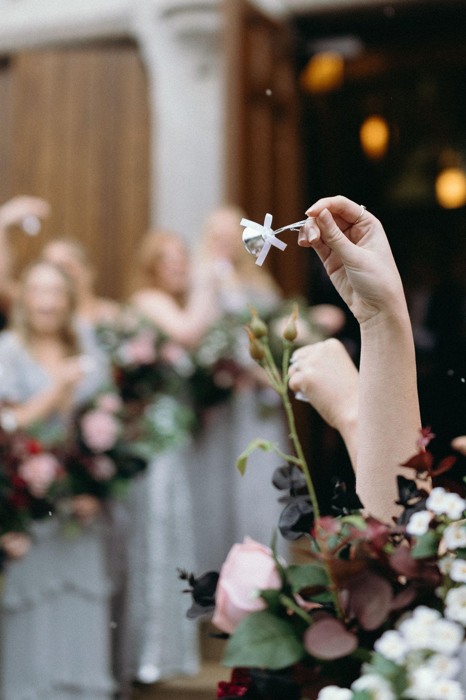 A hand holds a paper airplane against a blurred floral background at a wedding celebration.