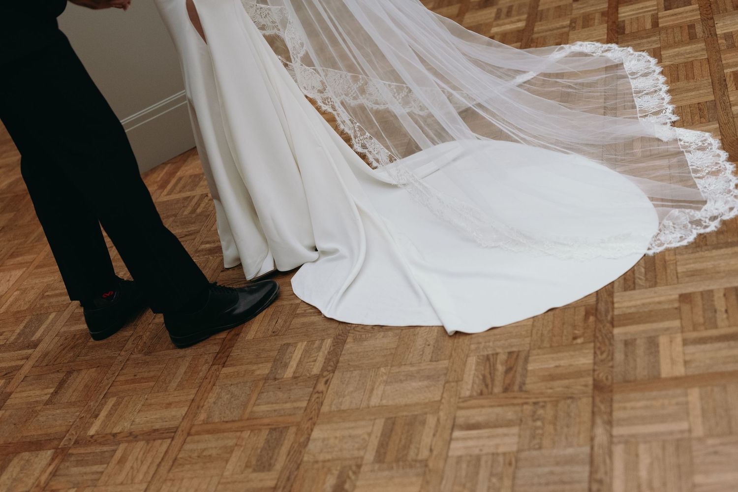 Close-up of wedding dress train and shoes on parquet flooring.