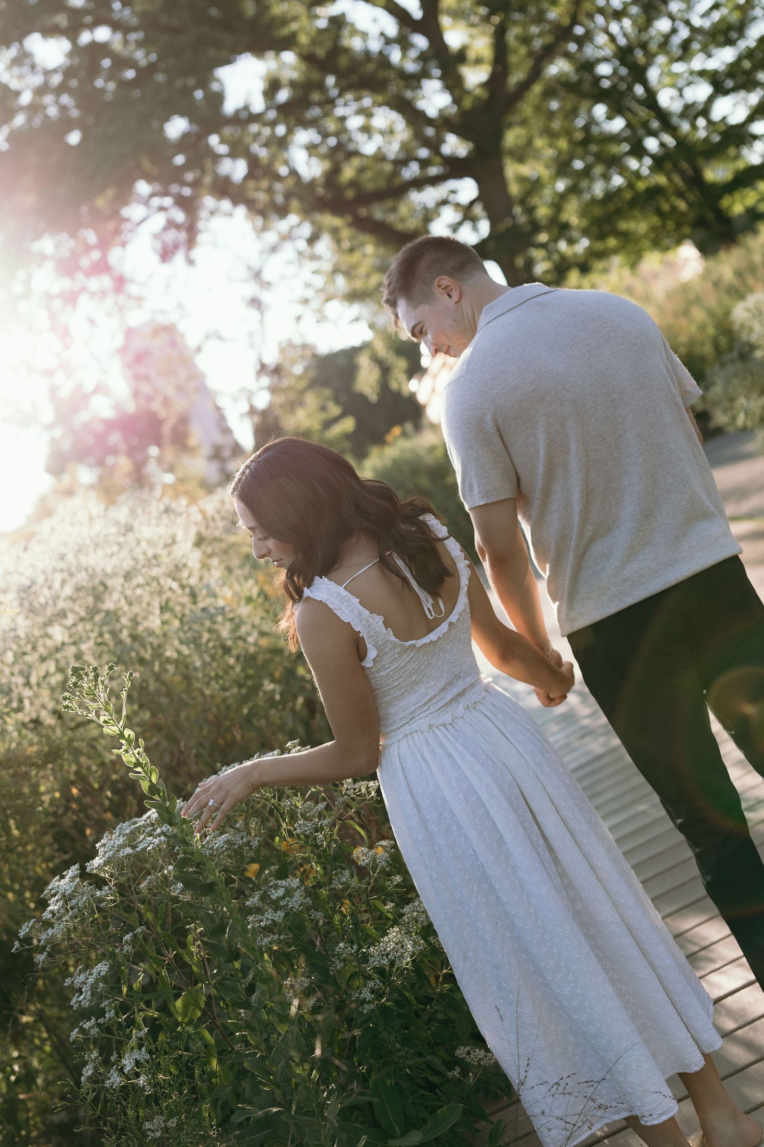 A couple in white and dark clothing share an intimate moment together in a sun-dappled garden setting.