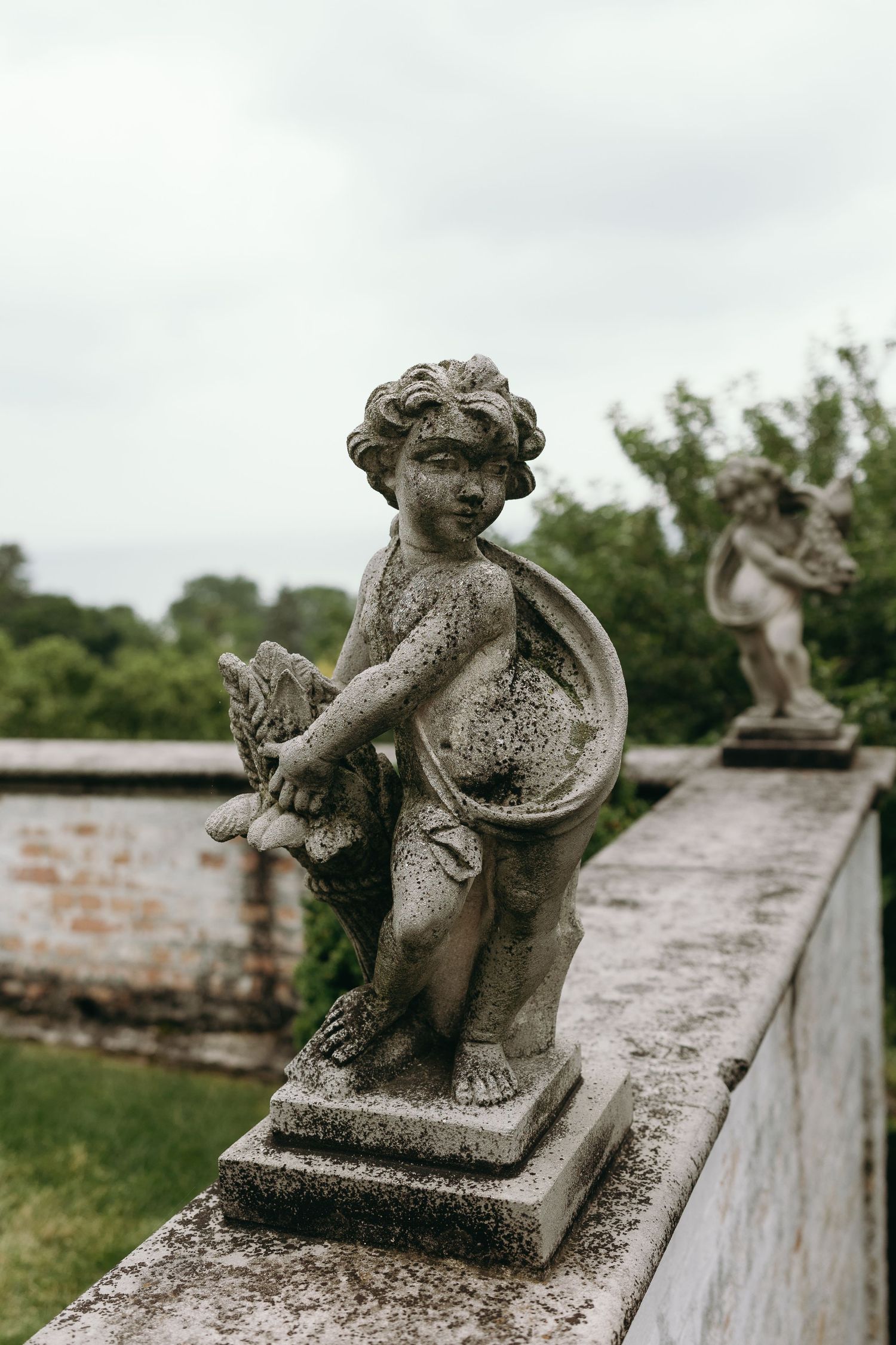Weathered stone cherub statues perched in a row along an old garden wall show signs of aging and patina.