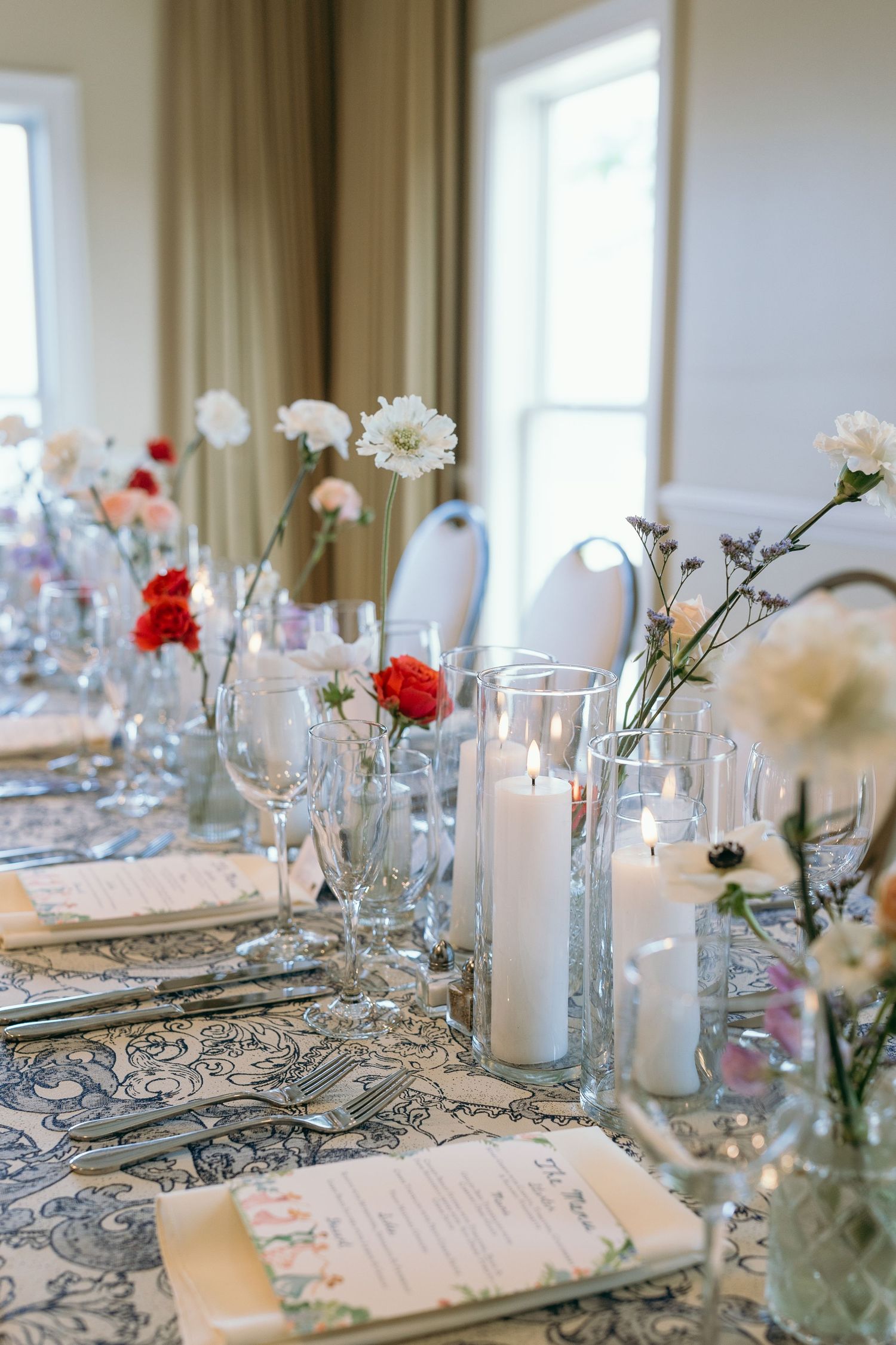 Elegant table setting with red and white flowers, tall candles, and patterned linens for a romantic dinner party.