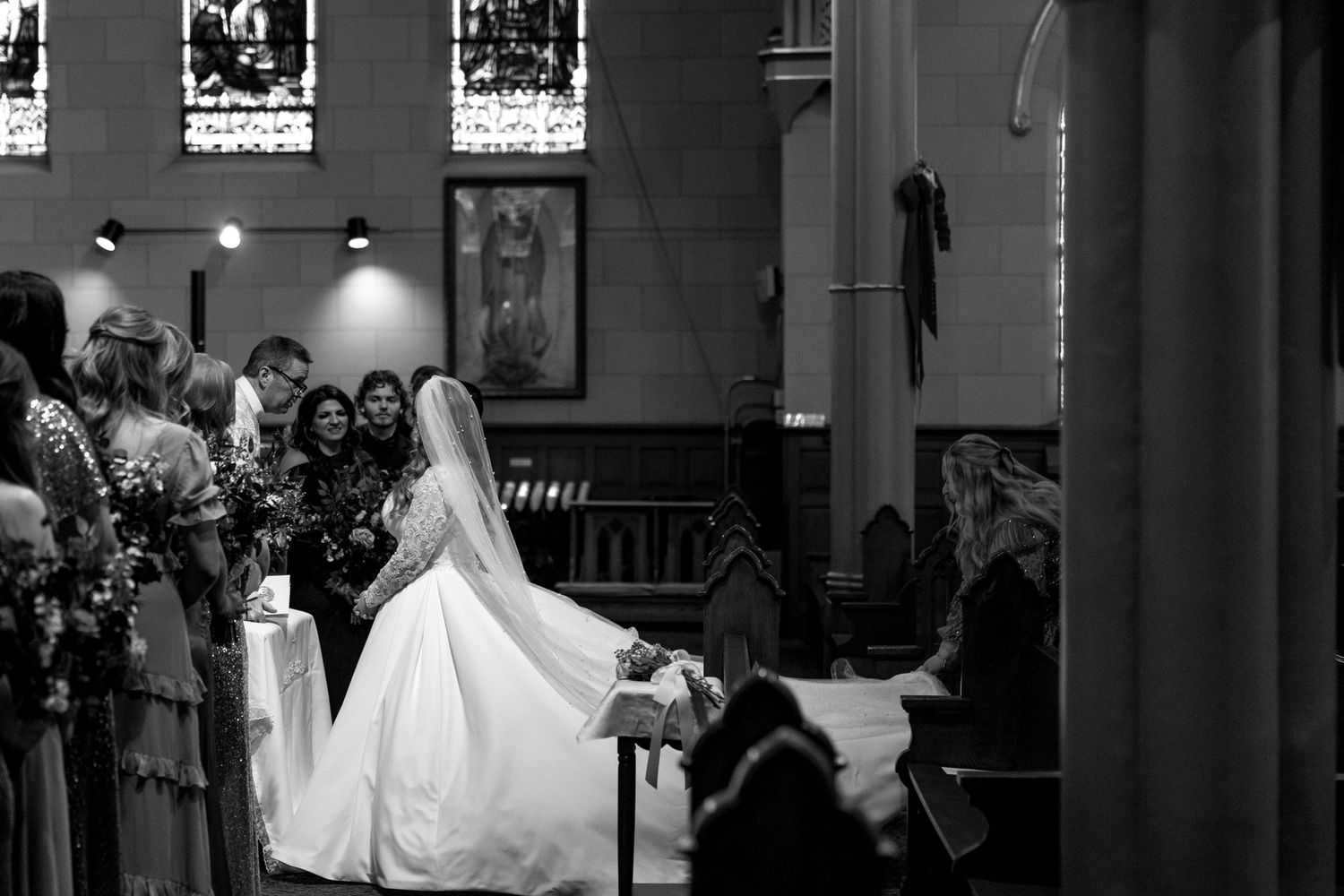 Black and white photograph of a bride in flowing white dress inside a classic church setting.