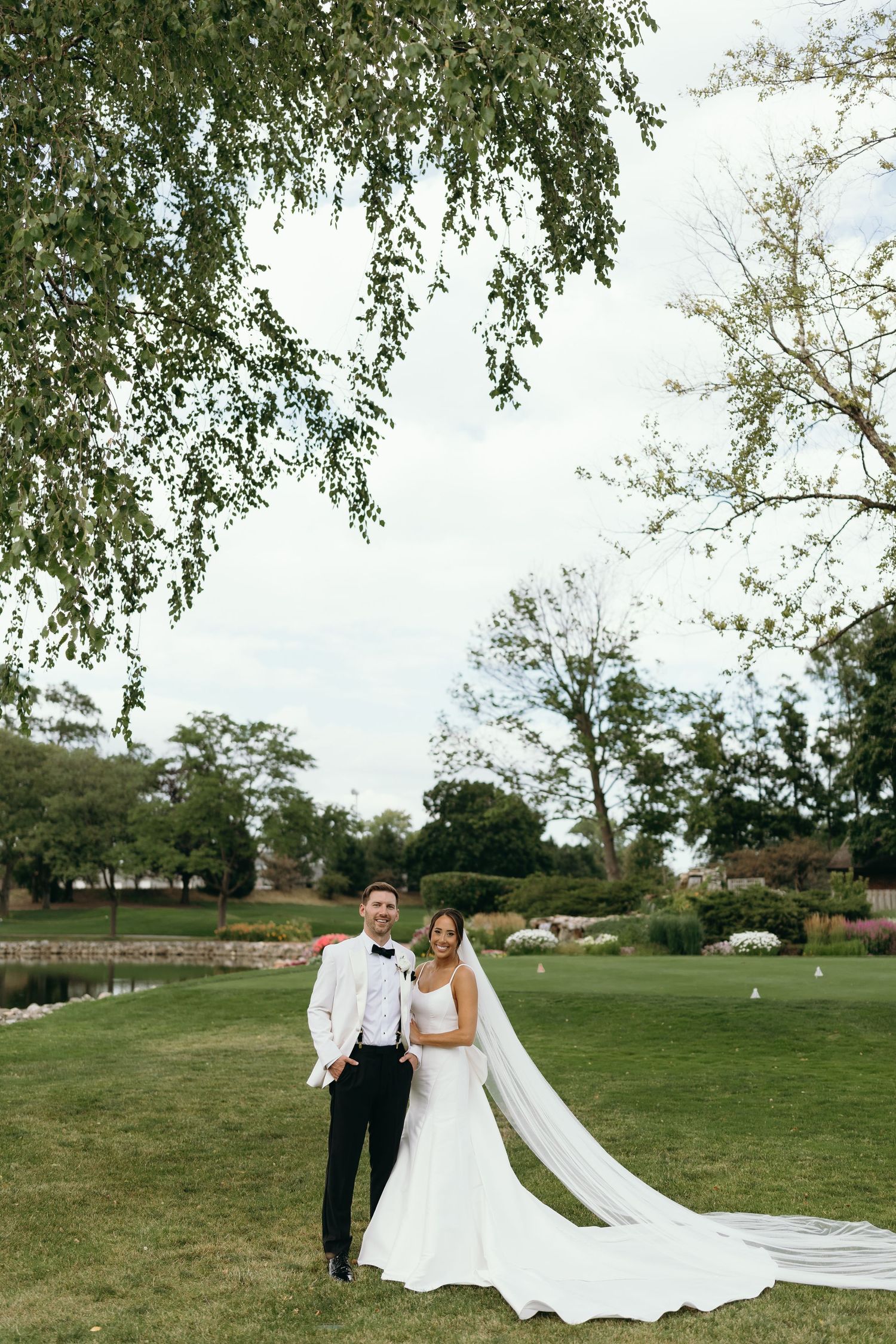 Newlyweds pose on a lush golf course with the bride's long veil flowing in the breeze.
