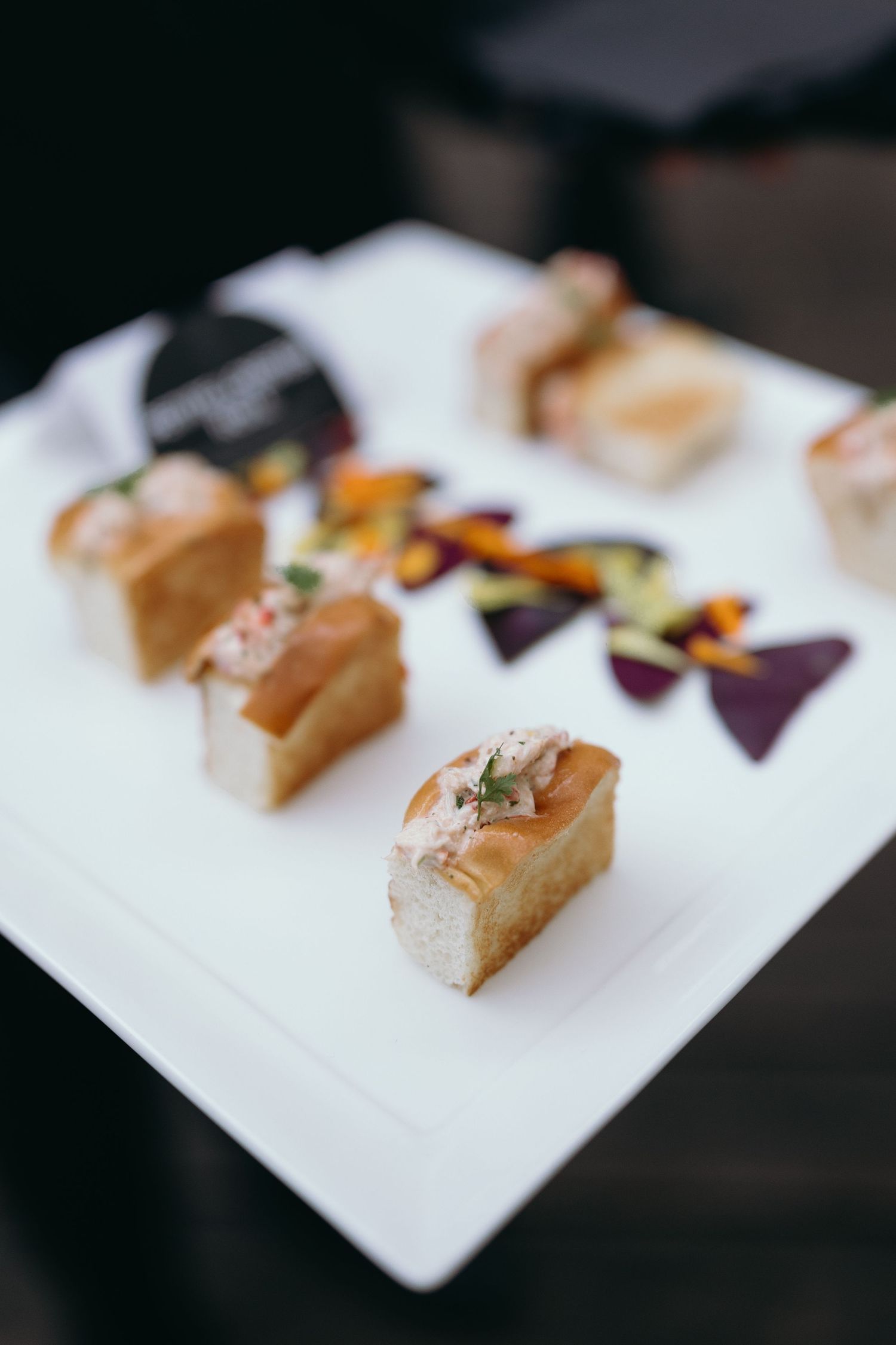 Small gourmet appetizers with garnishes arranged on a white plate.