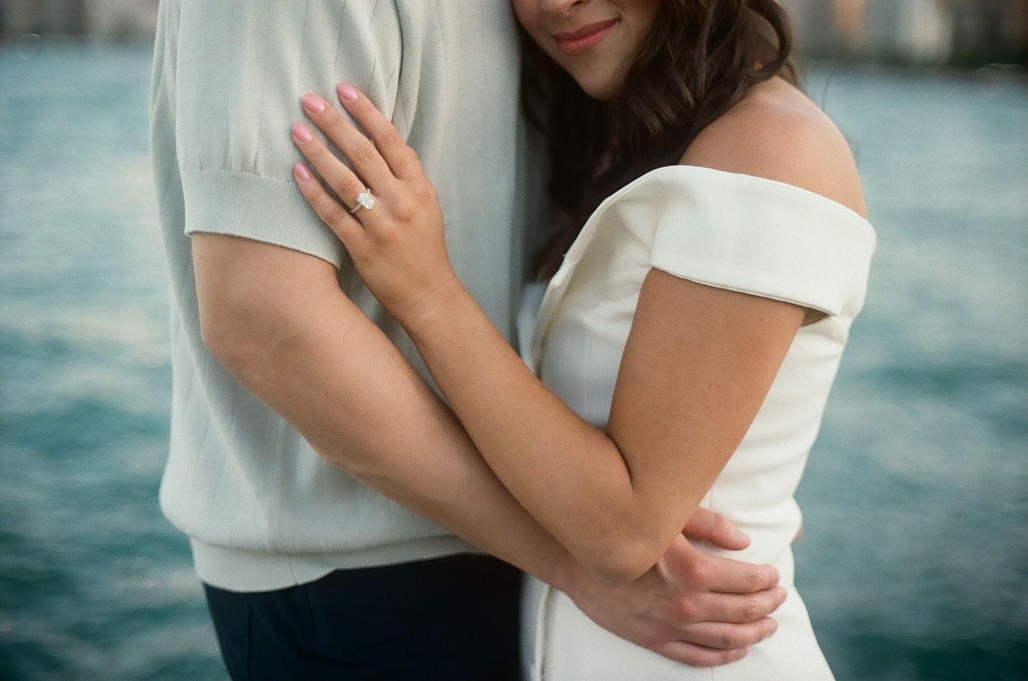 A romantic close-up photo series of a couple embracing outdoors by the water in white clothing.