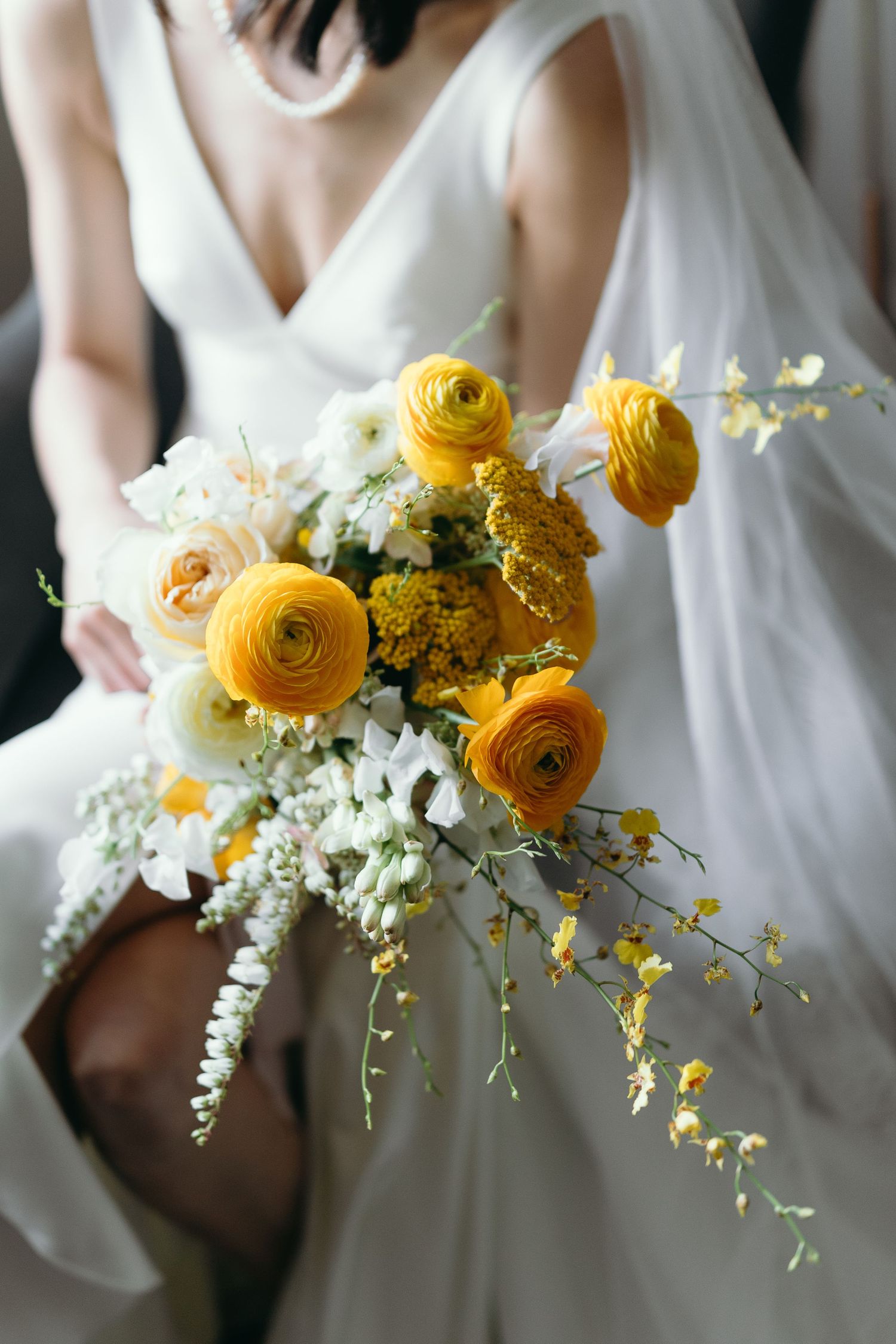 Elegant bridal bouquet with yellow ranunculus flowers and white orchids against white dress.