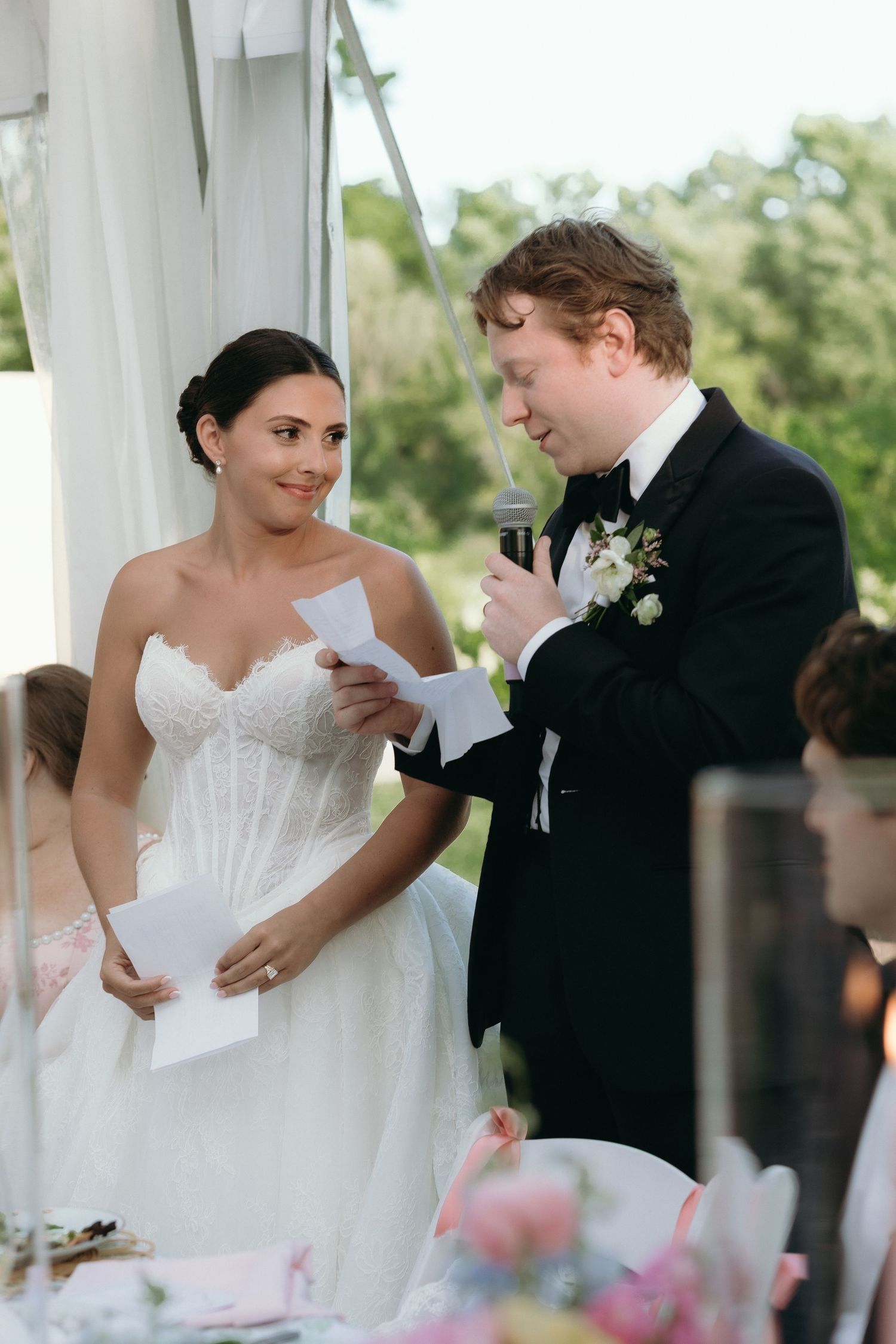 Bride and groom reading vows at outdoor wedding reception under white tent.