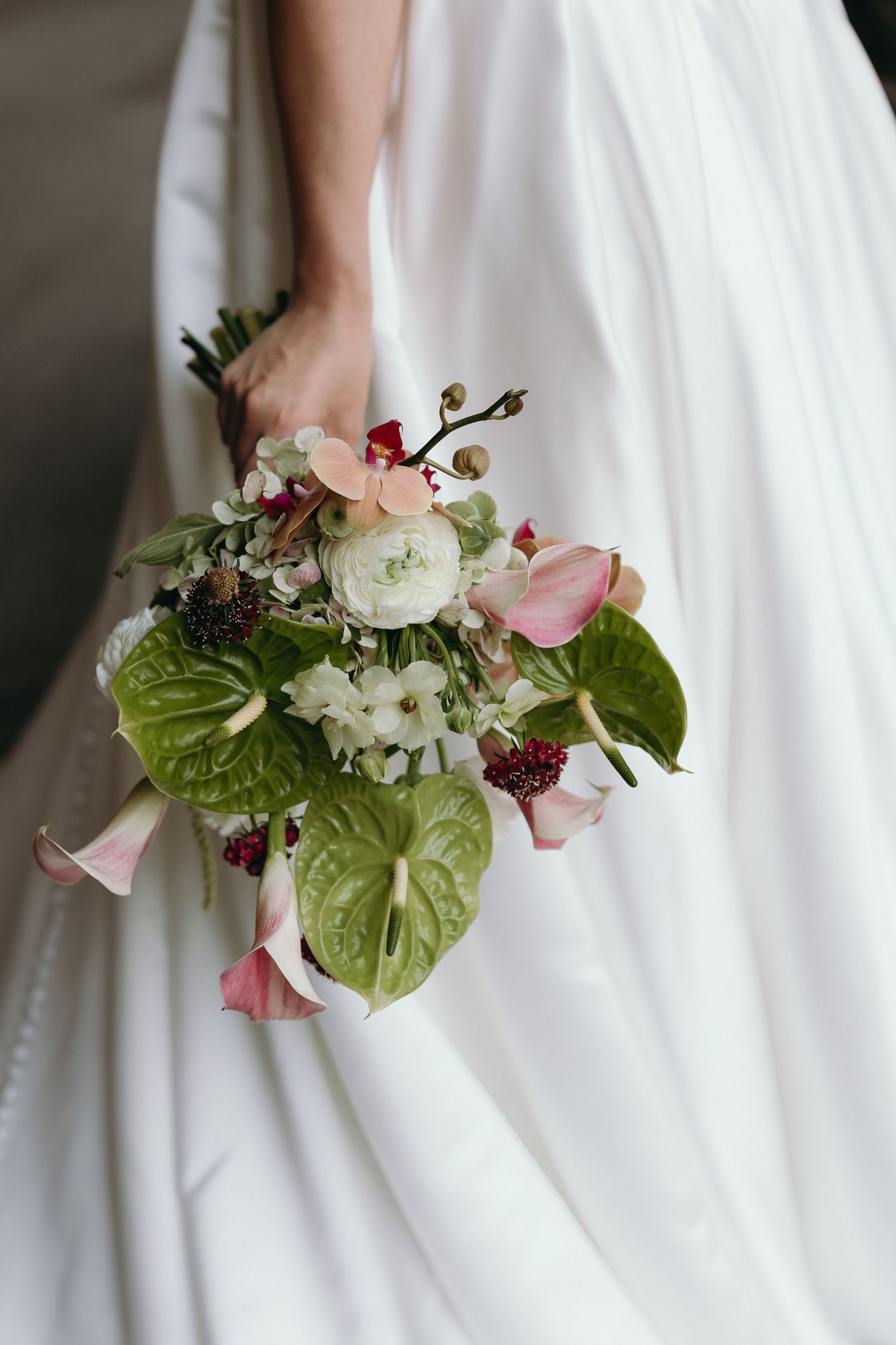 A series of wedding bouquet details featuring pink calla lilies, white ranunculus, and green anthurium leaves against a white dress.