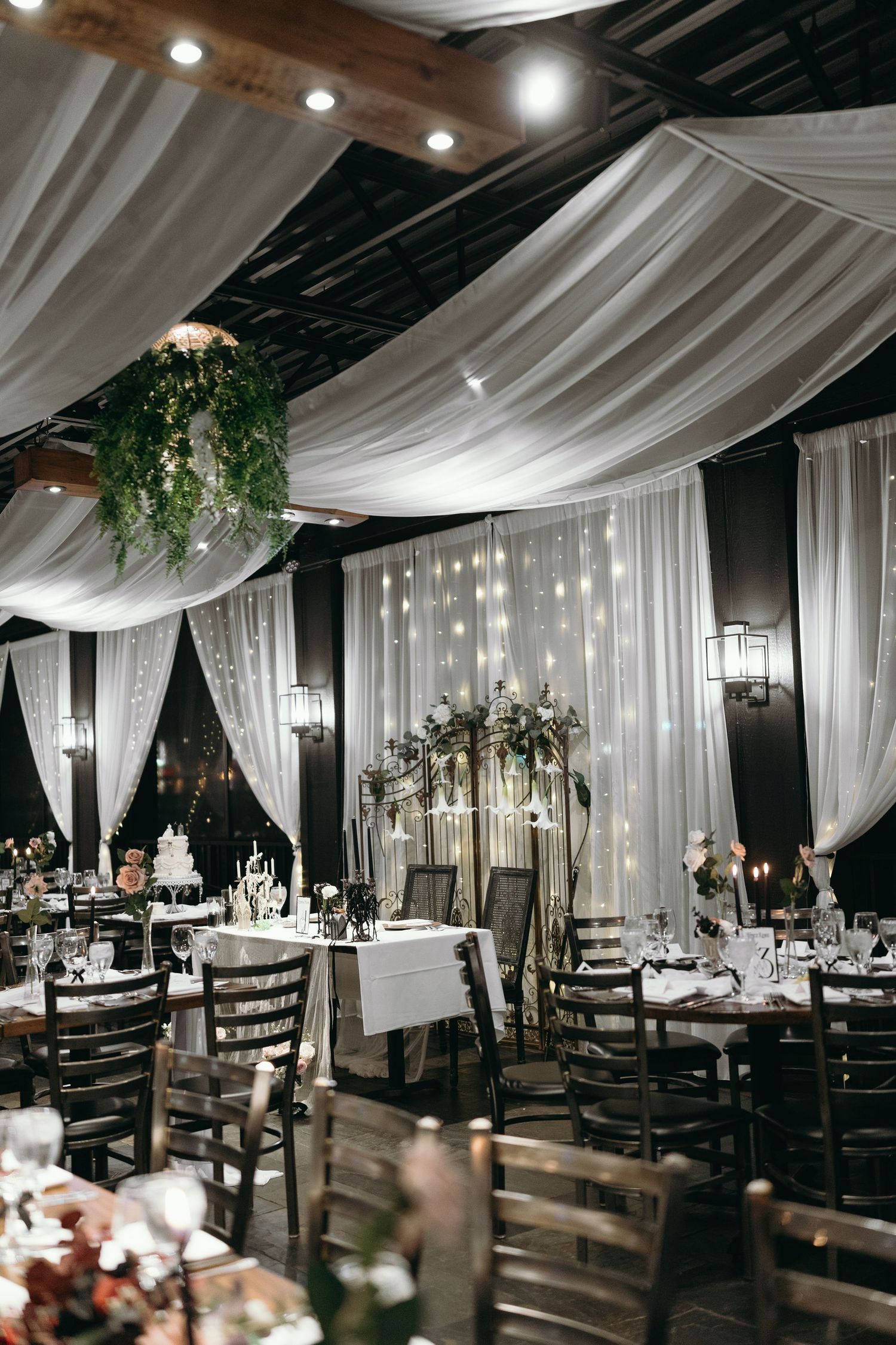 Romantic wedding reception venue with draped white fabric, twinkling lights, and elegant table settings.