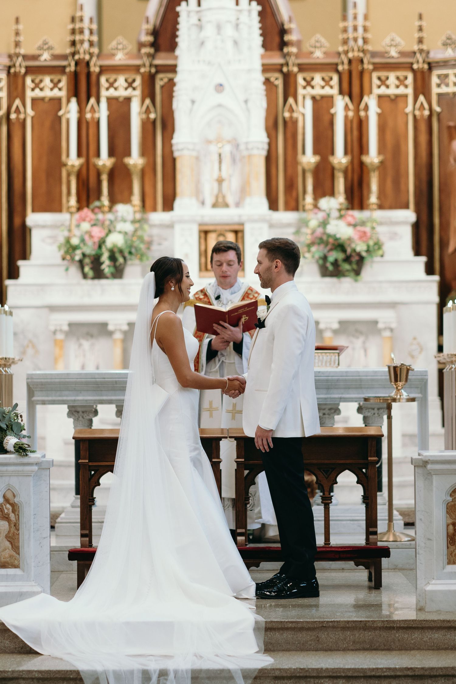 Wedding ceremony in progress at ornate church altar with white and gold details.