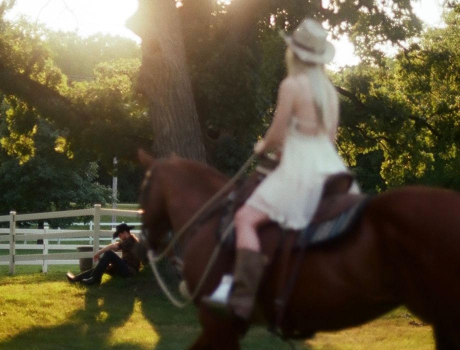A person rides horseback in silhouette against a brilliant golden sunset with white fences visible in the background.