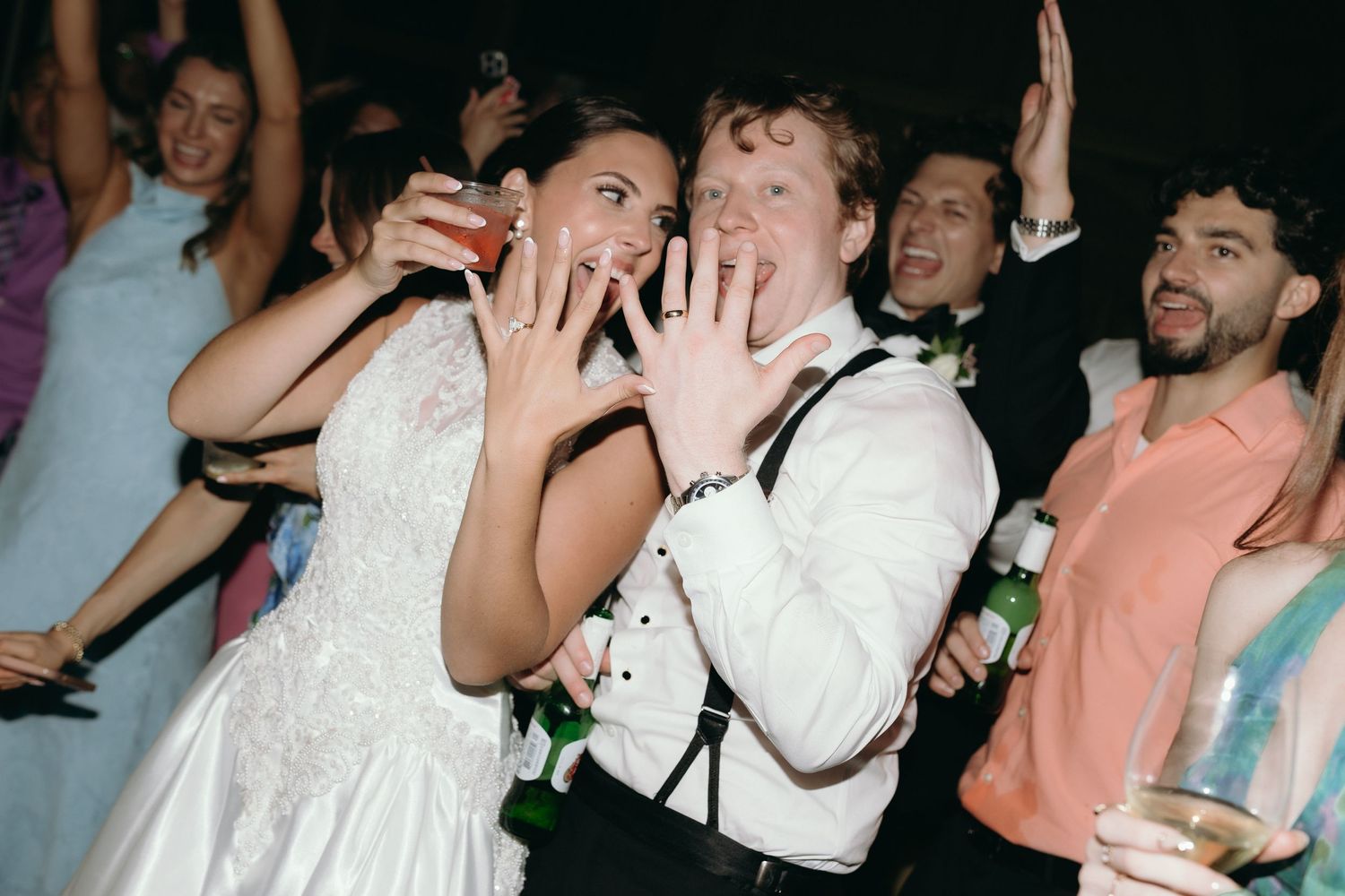 Bride and groom showing off wedding rings while celebrating with guests on the dance floor.