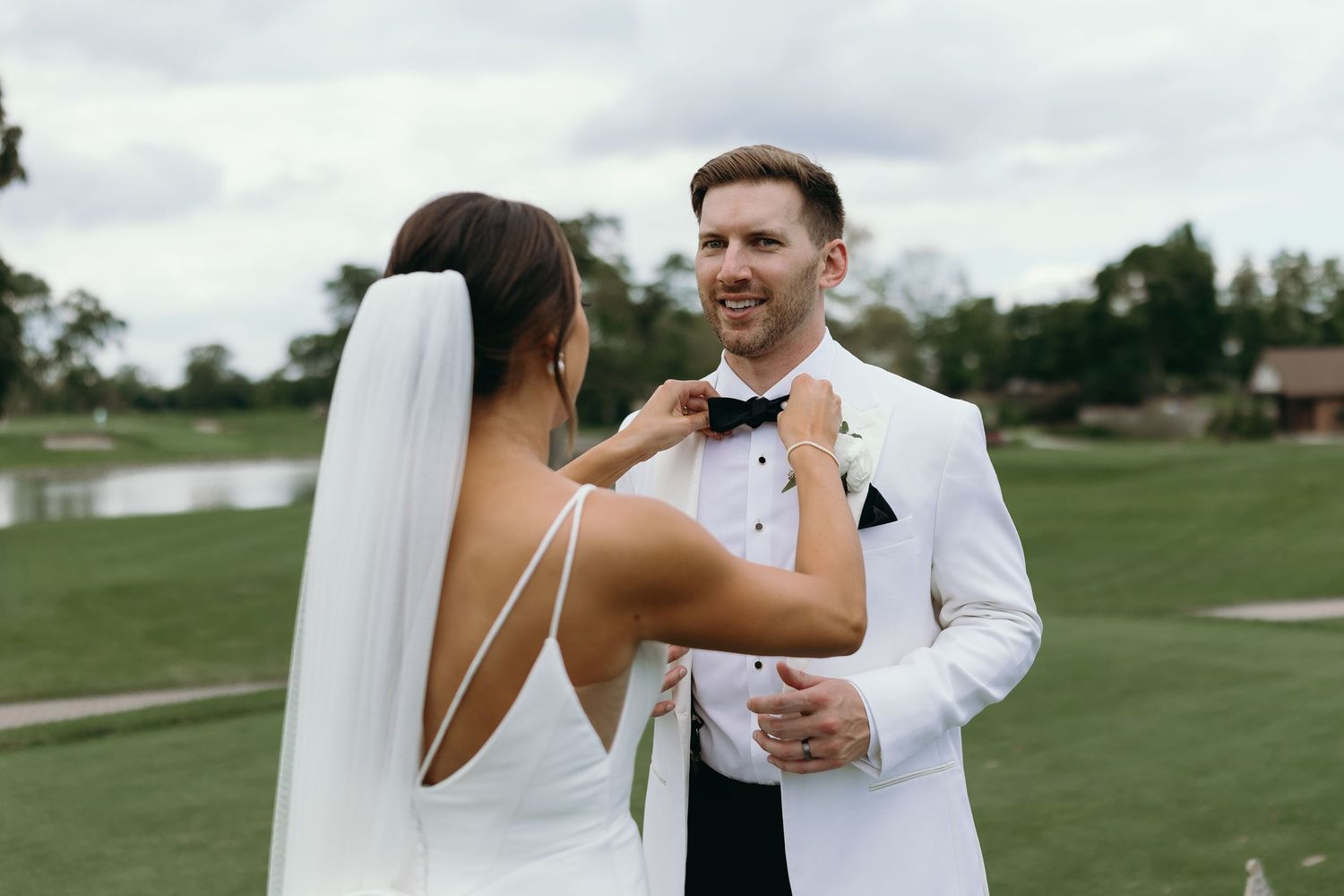 Wedding couple shares a candid moment on a grassy lawn.