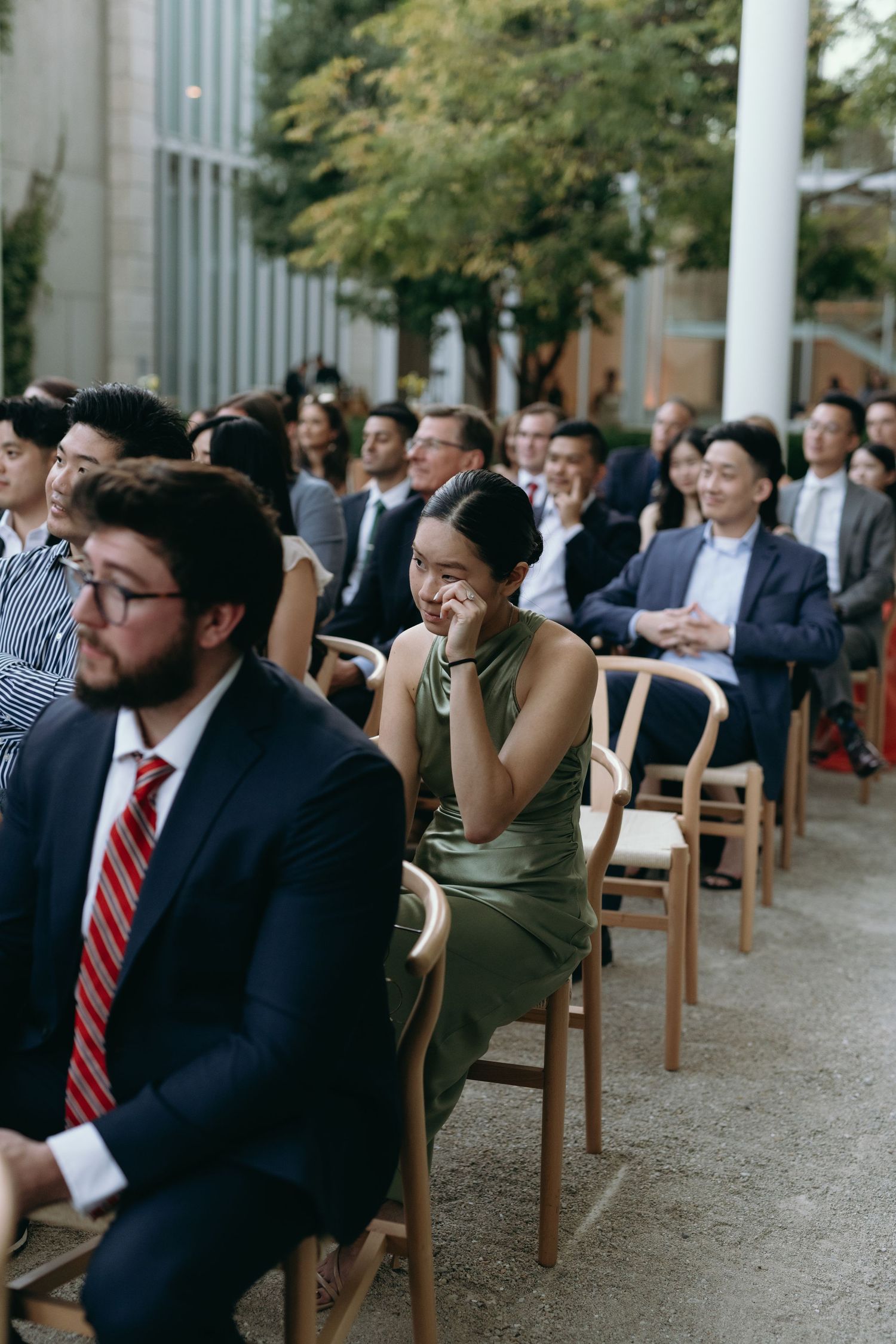 Wedding guests seated in rows of wooden chairs at an outdoor ceremony.