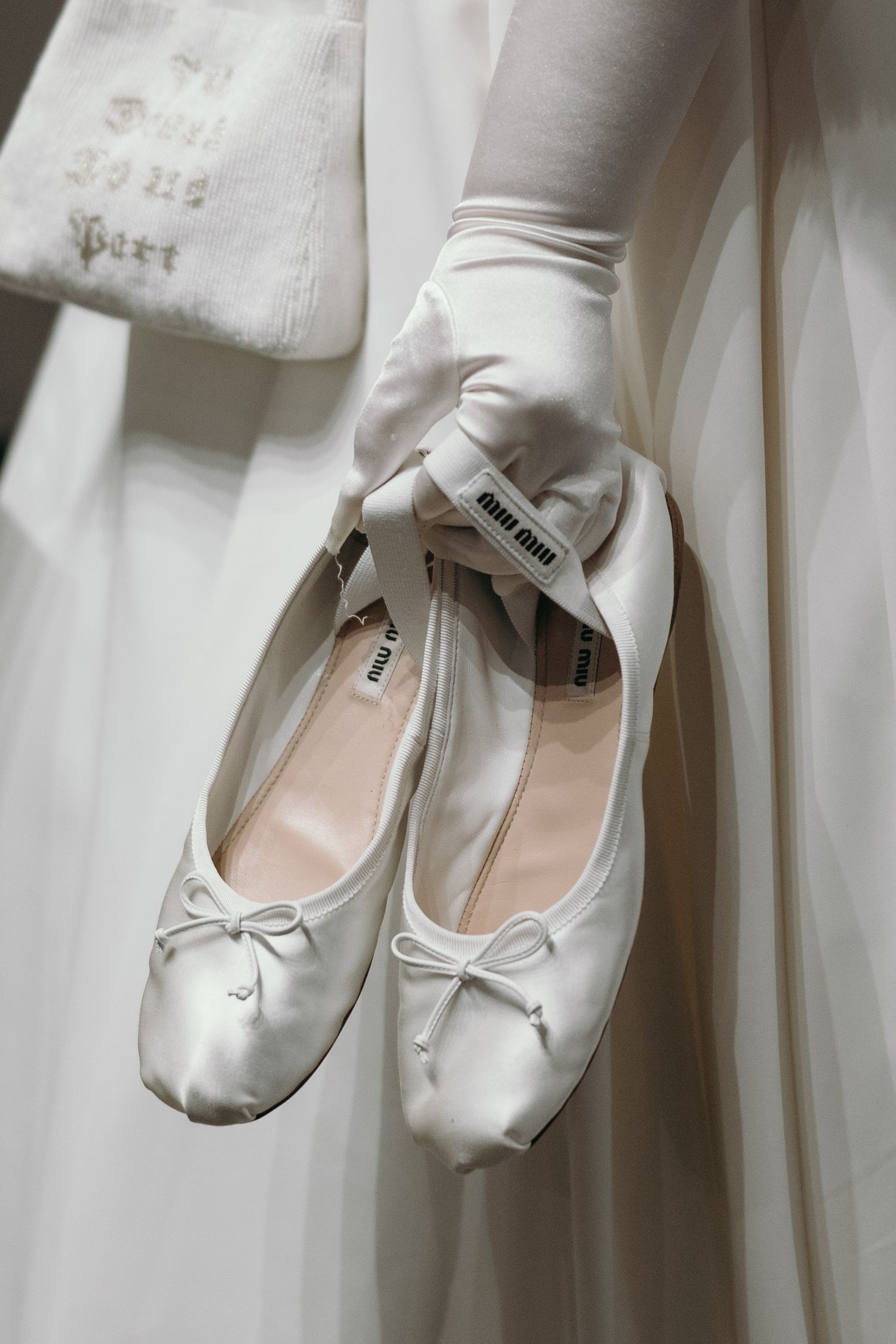 White ballet slippers hanging delicately against white fabric backdrop.