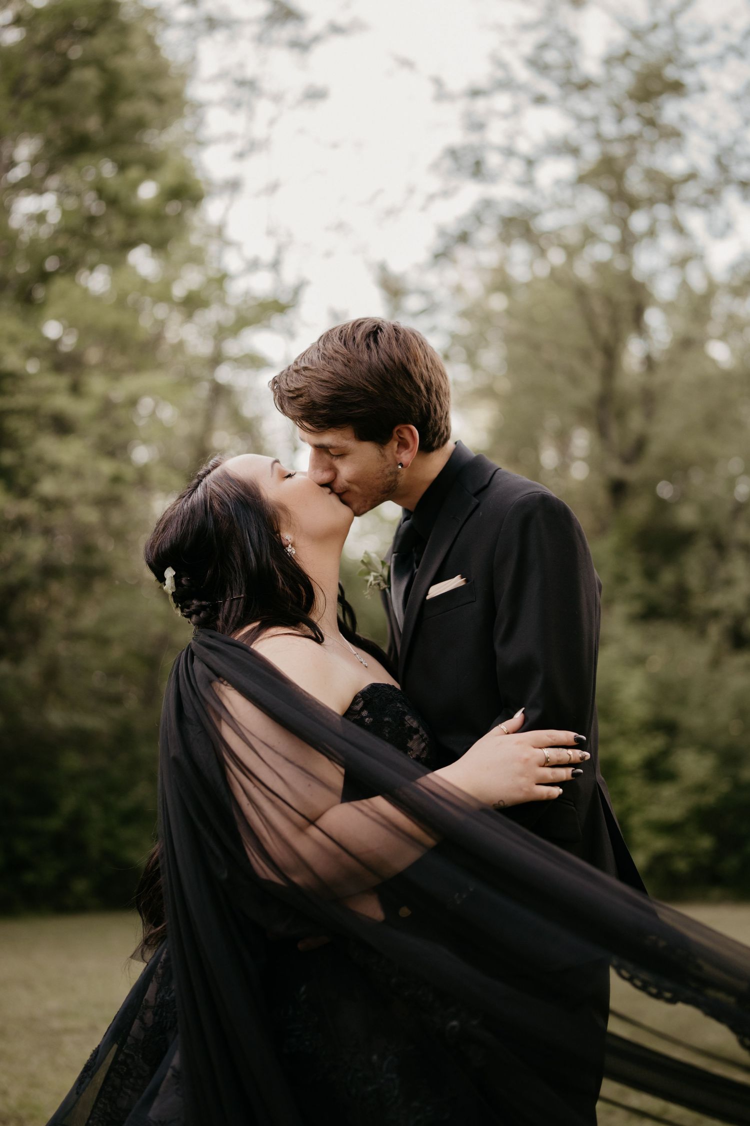 A romantic couple in formal attire embraces in an outdoor photoshoot.