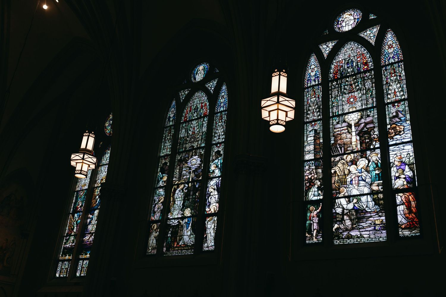 Row of stained glass windows in a dark cathedral setting.