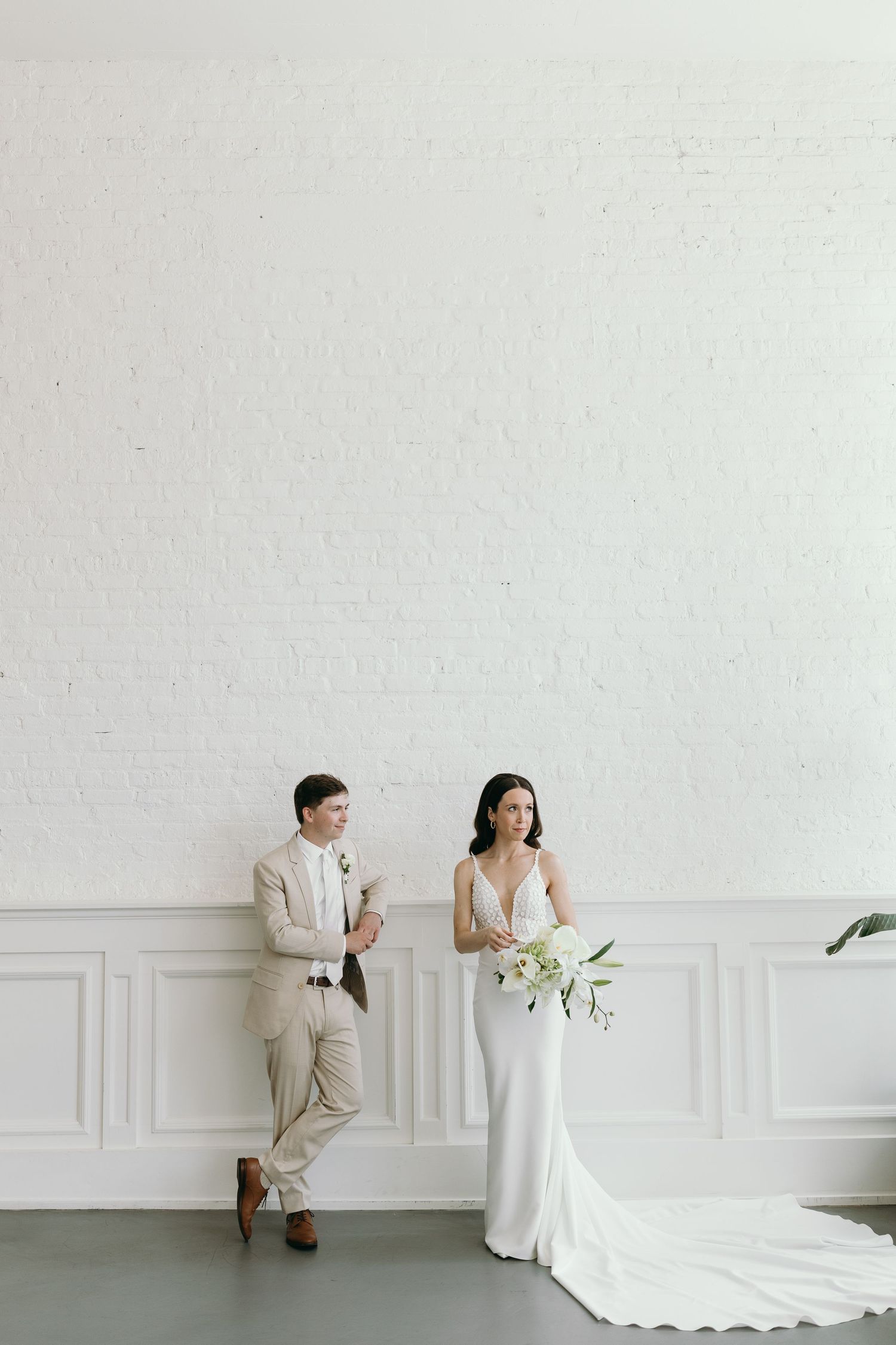 Modern wedding portrait of couple against white wall with classic architectural details.