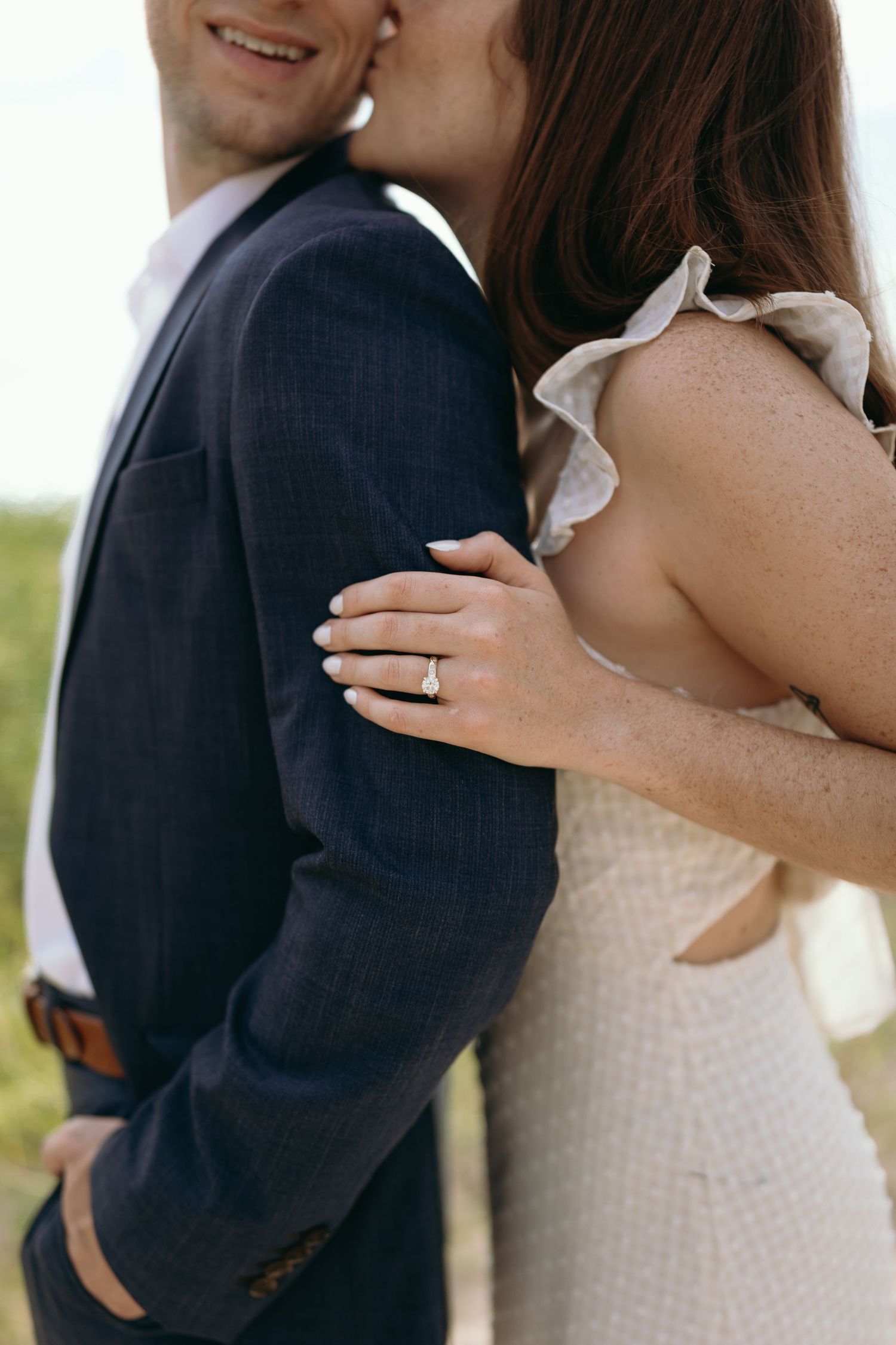 Close-up of a couple embracing outdoors, showing the bride's engagement ring against a navy suit.